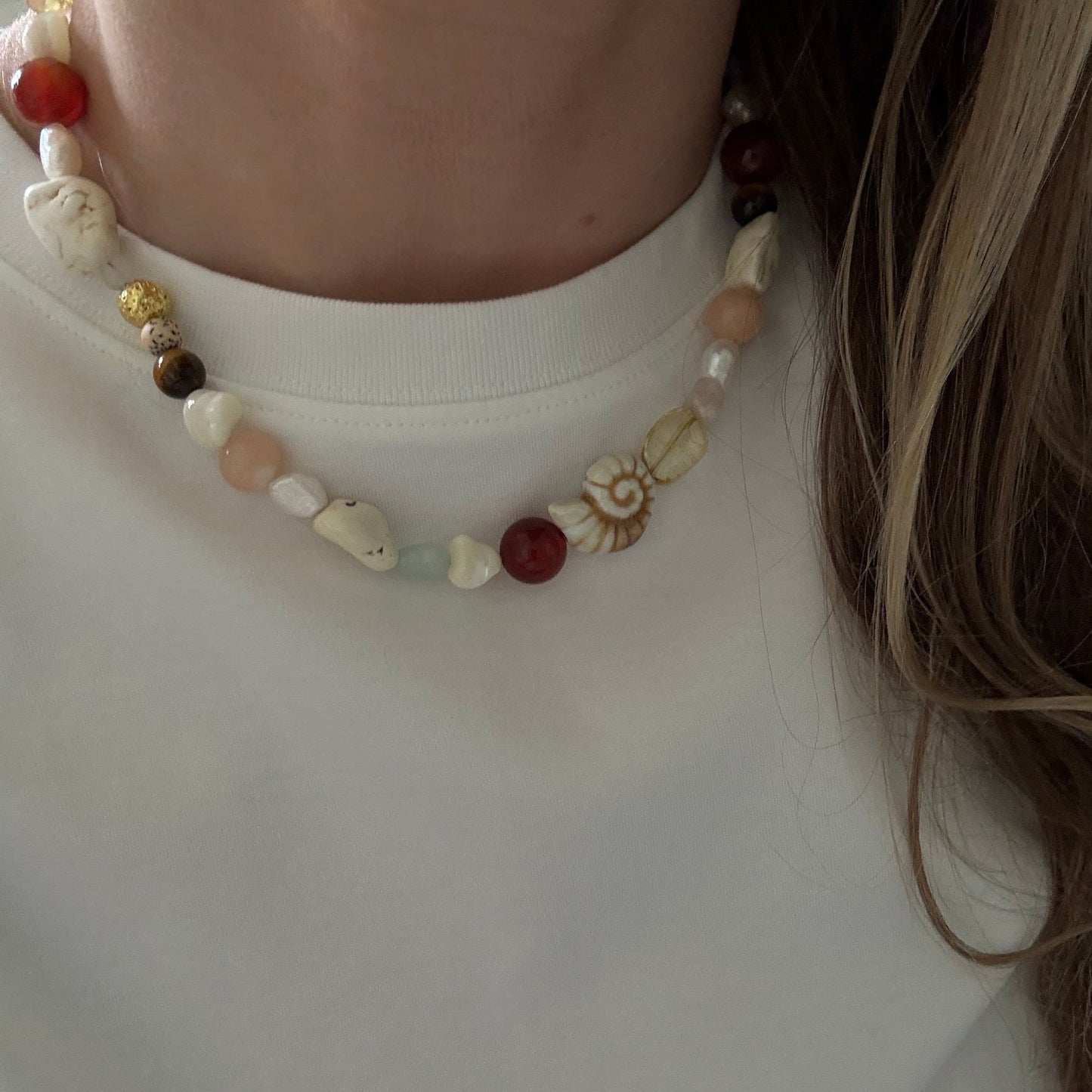 Necklace with multicolored beads worn by a person on a plain background