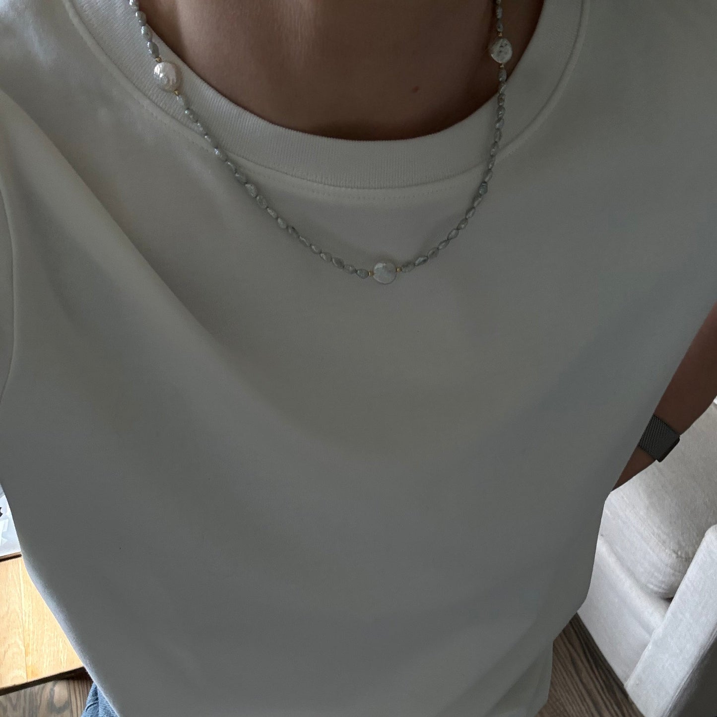 White sleeveless top with pearl details worn by a person, sitting on a wooden floor.