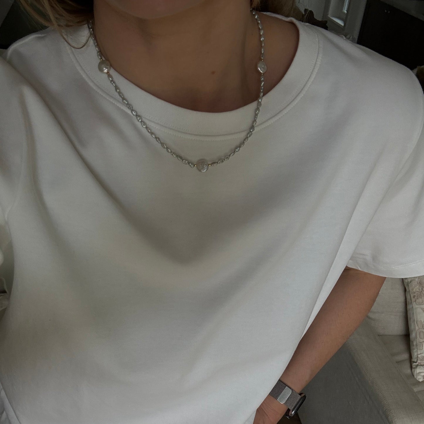 Person wearing a white shirt and blue jeans sitting on a couch.