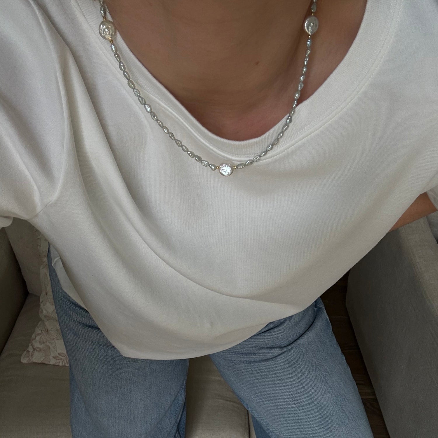 Person wearing a white top and blue jeans sitting on a couch.
