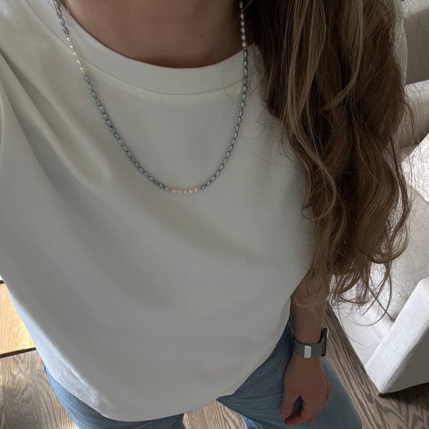 Person wearing a white top and blue jeans on a wooden floor.