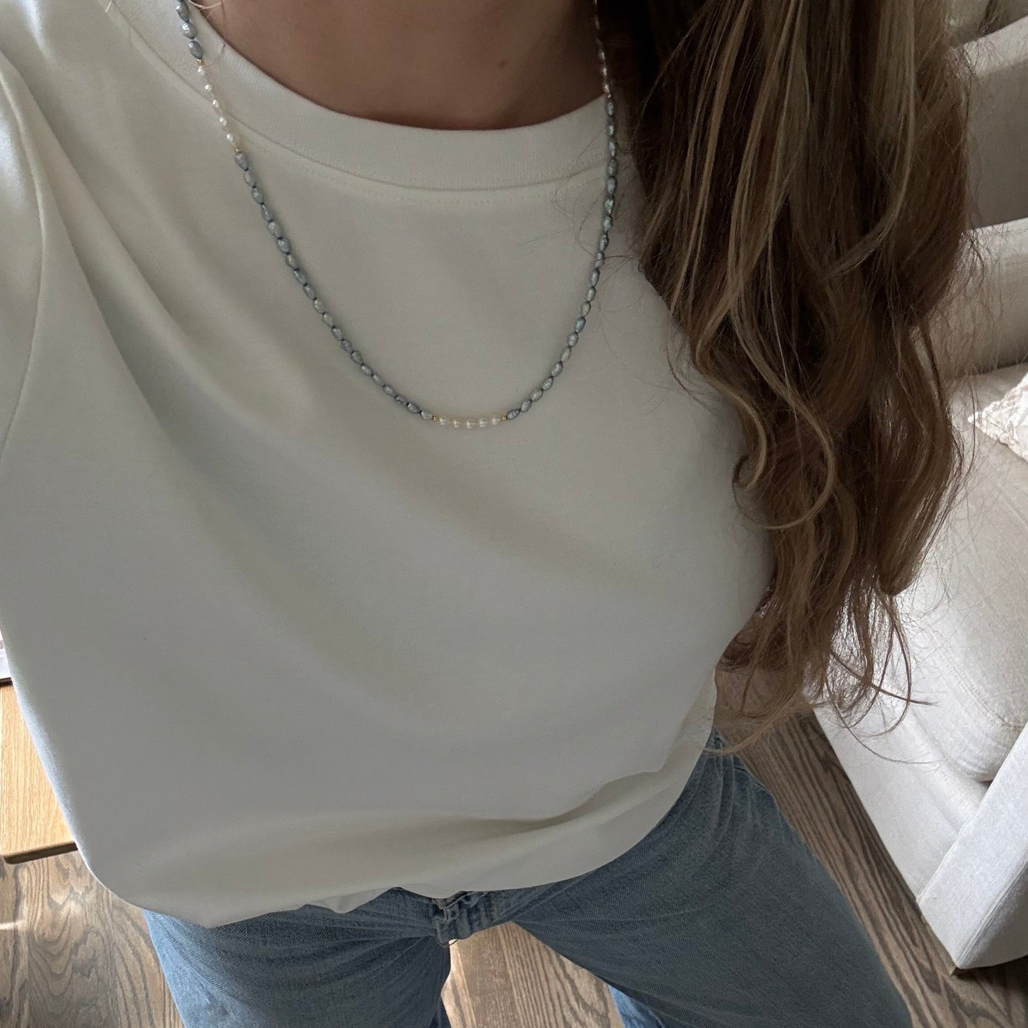 Person wearing a white top with embellishments and blue jeans on a wooden floor.