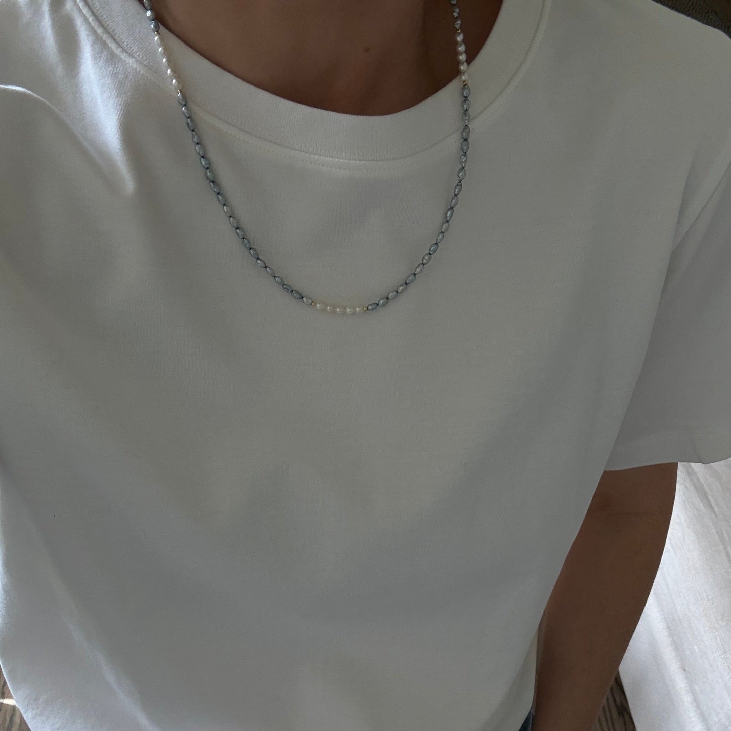 Person wearing a white sleeveless top with a necklace, sitting on a couch.