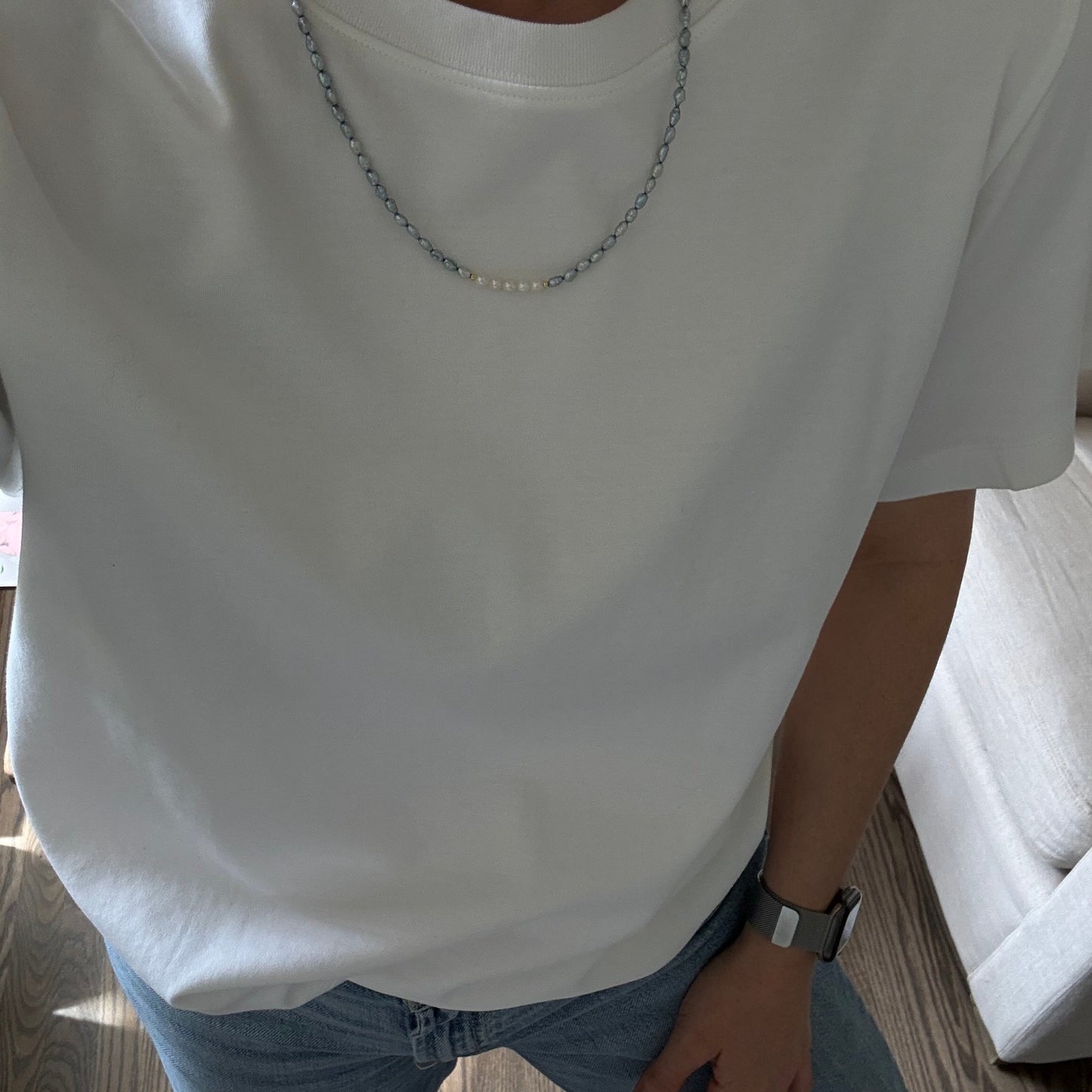 Person wearing a white sleeveless top and blue jeans sitting on a wooden floor.