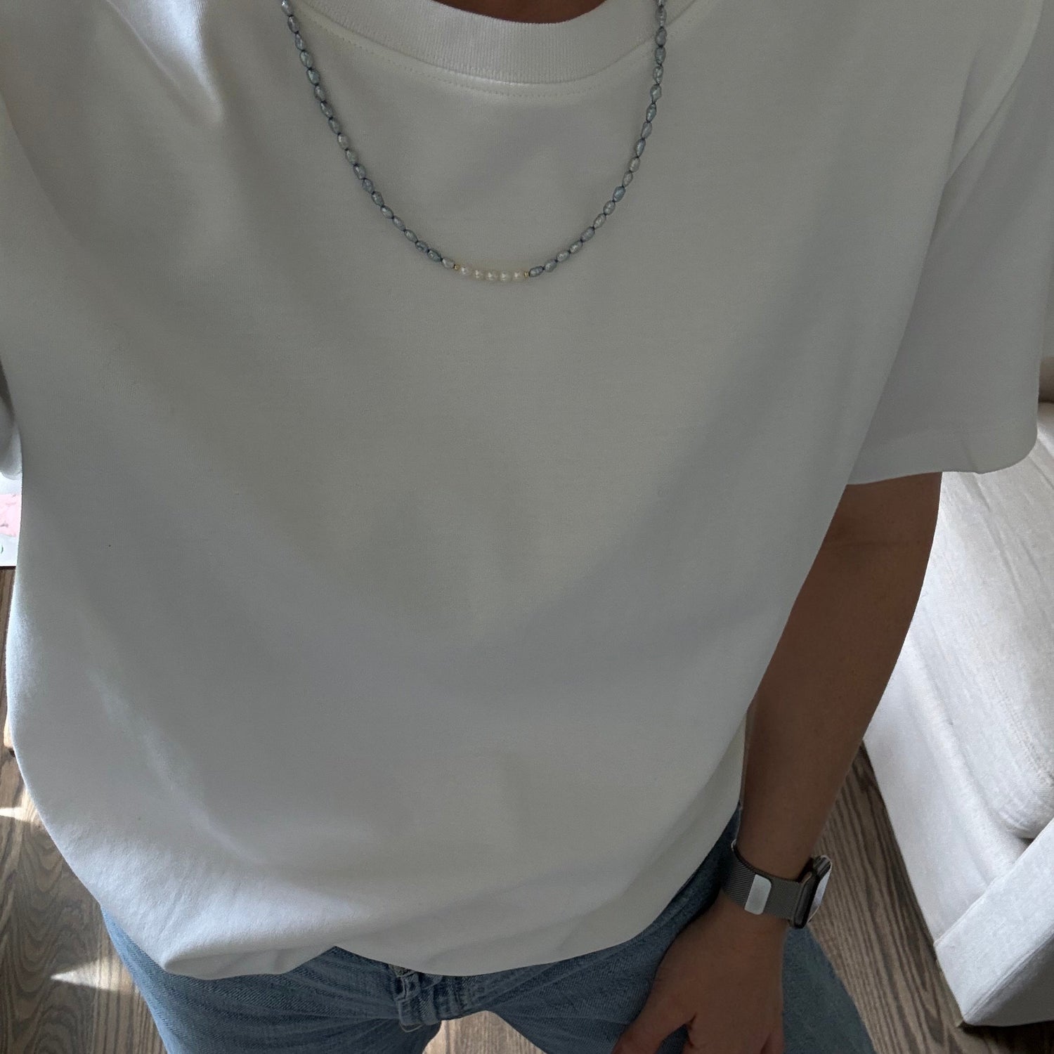 Person wearing a white sleeveless top and blue jeans sitting on a wooden floor.