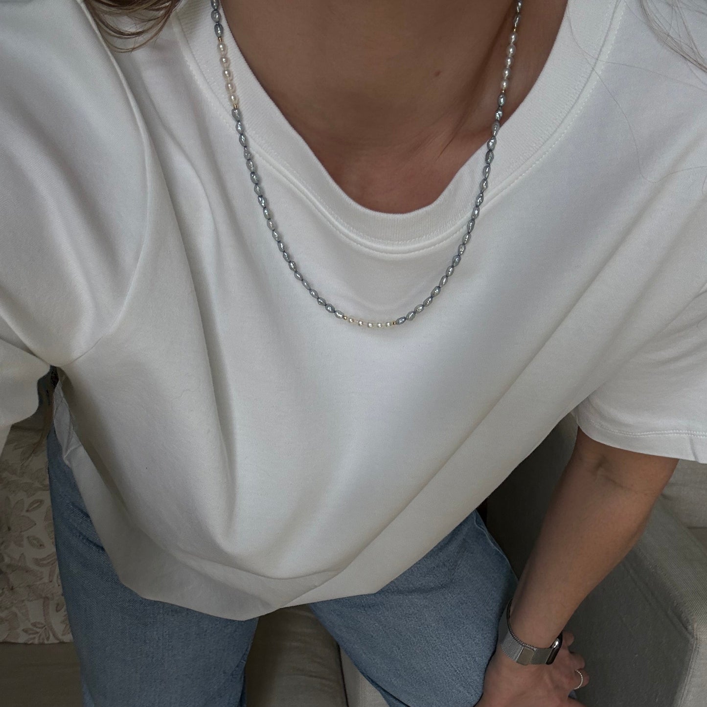 Person wearing a white shirt and blue jeans sitting on a couch.