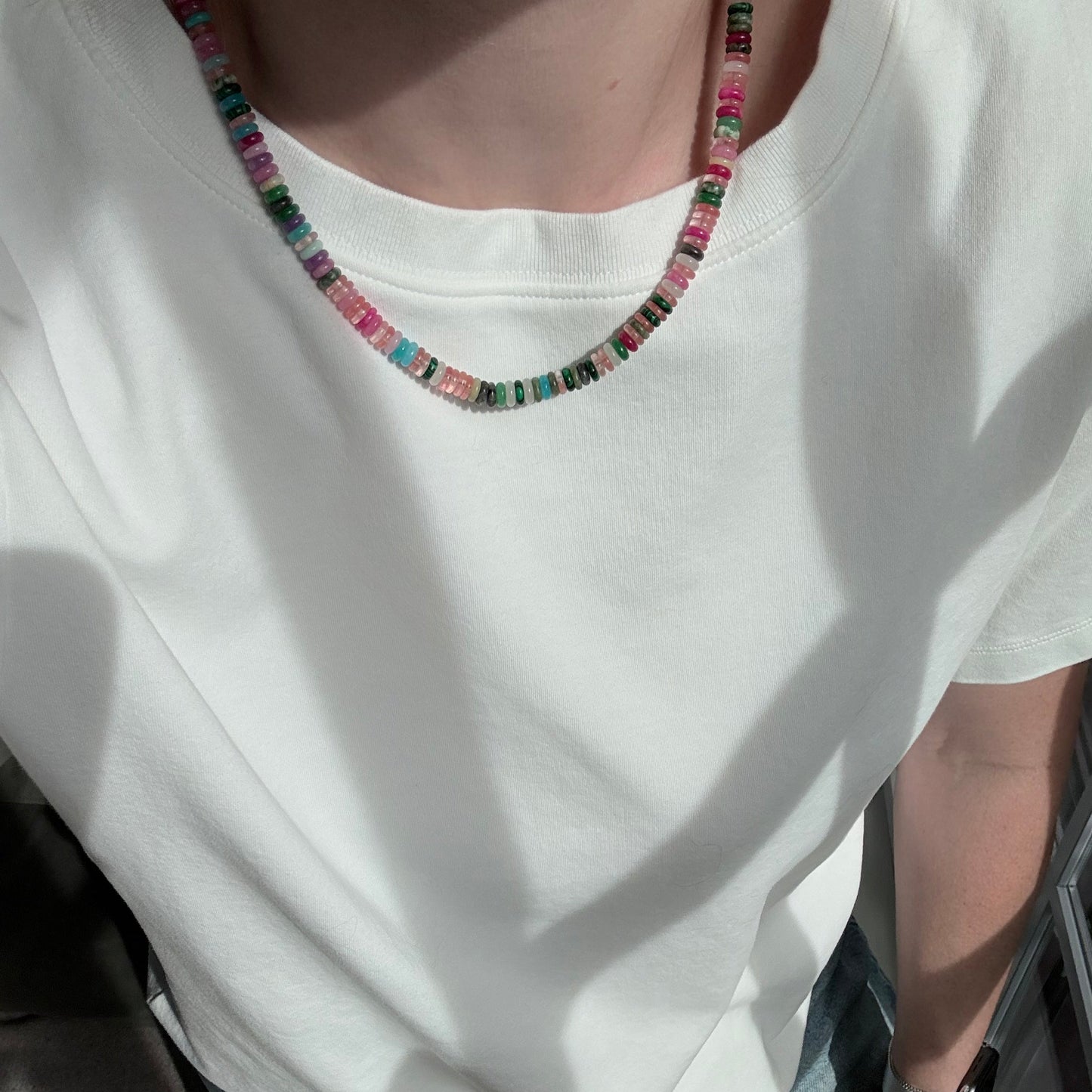 Person wearing a white tank top with colorful beaded necklace inside a vehicle.