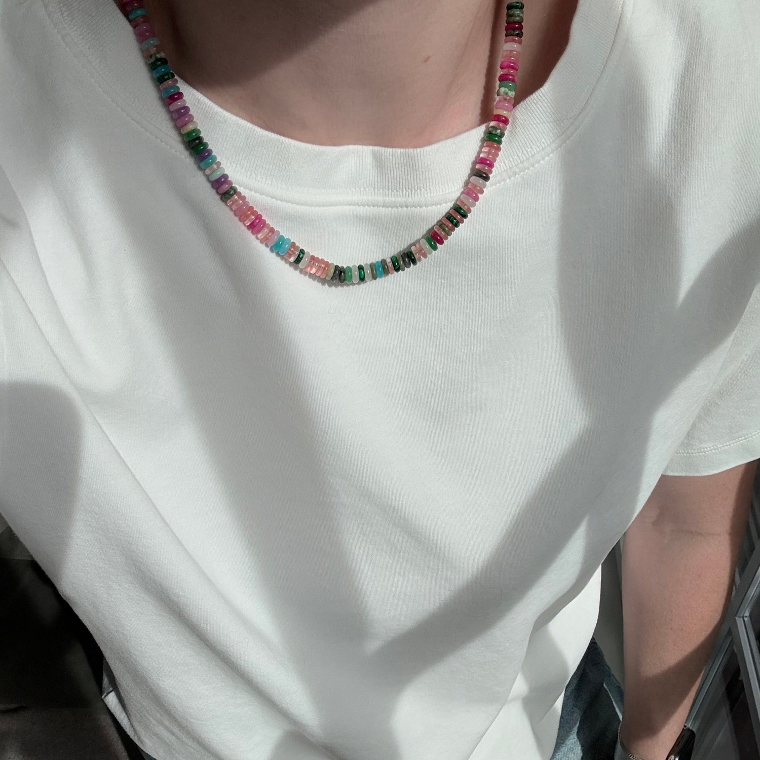 Person wearing a white tank top with colorful beaded necklace inside a vehicle.