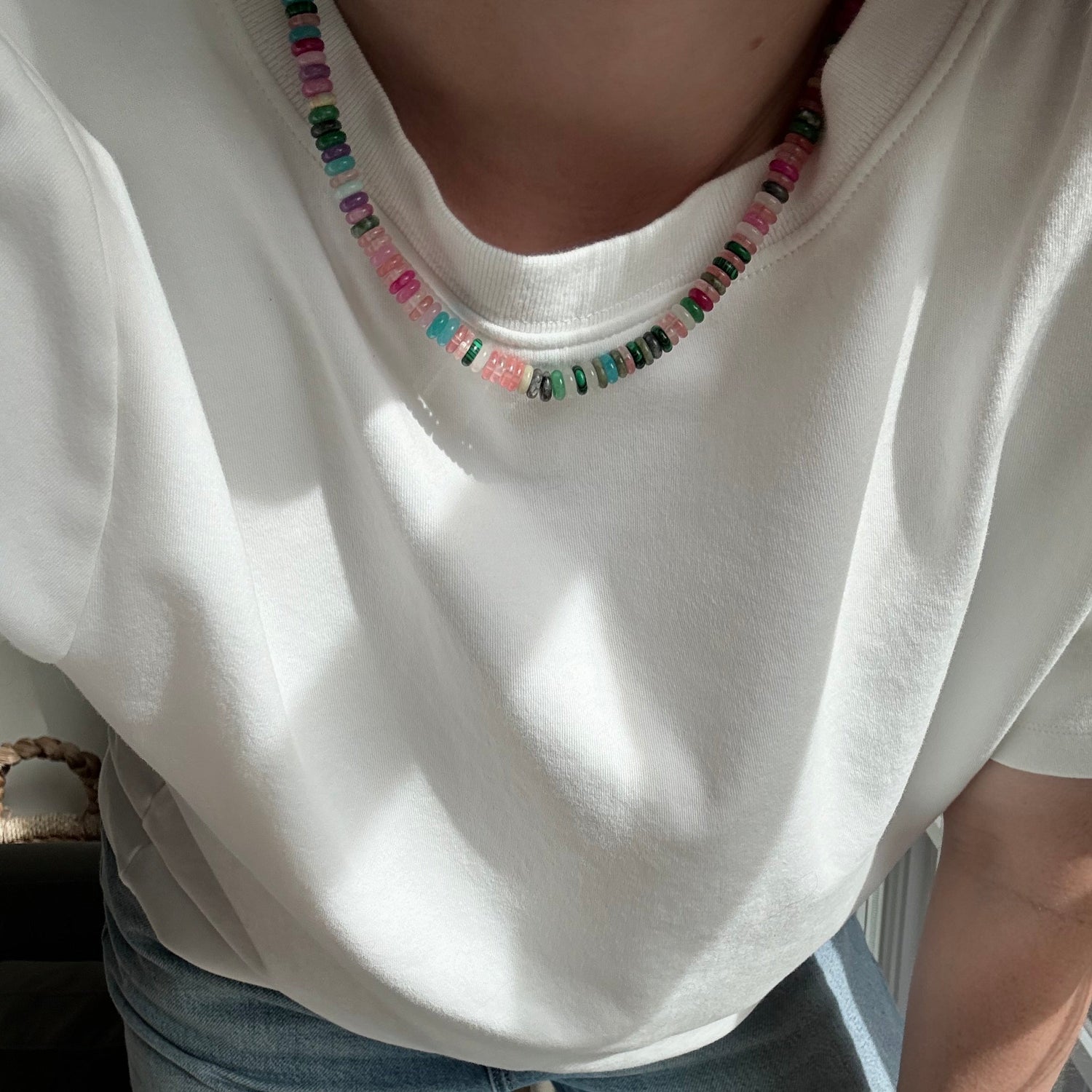 Person wearing a white top with colorful embellishments and light blue jeans sitting on a bench.
