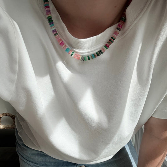 Person wearing a white top with colorful embellishments and light blue jeans sitting on a bench.