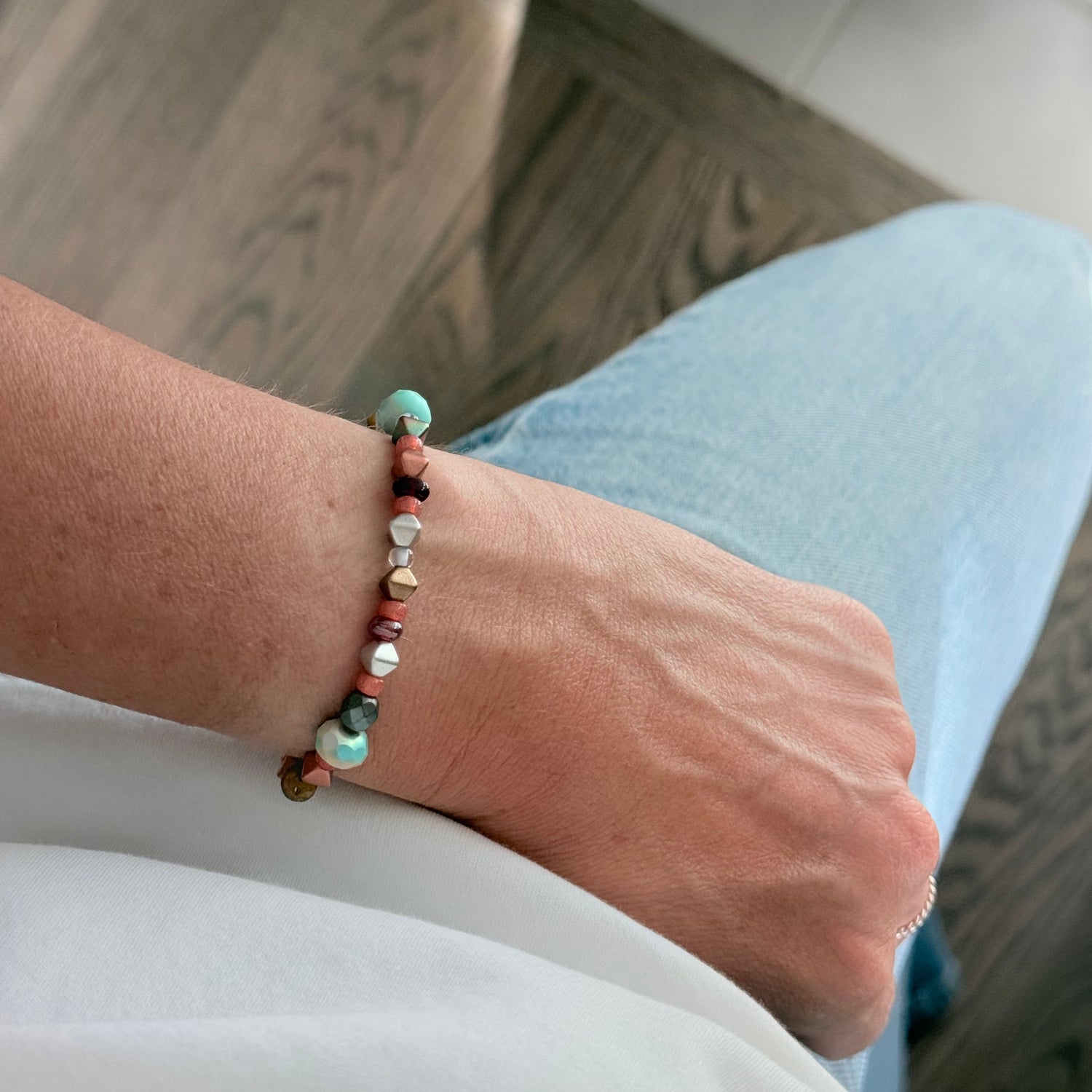 Close-up of a wrist wearing a colorful beaded bracelet on a blurred indoor background