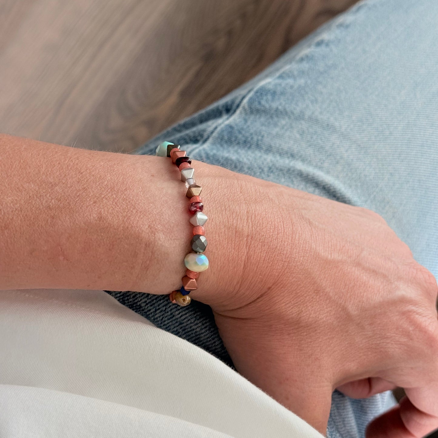 Close-up of a hand wearing a beaded bracelet on a wooden floor.