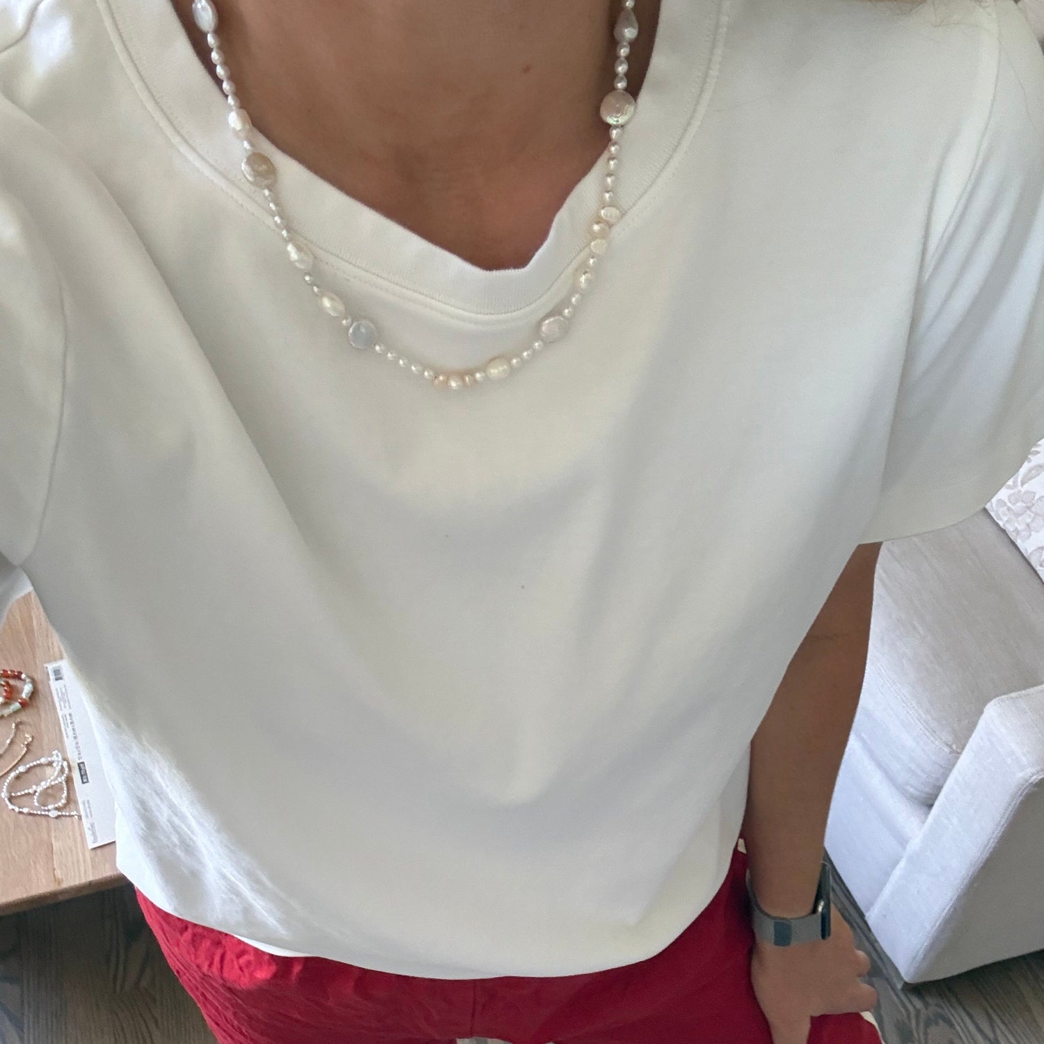 Person wearing a white dress with a pearl necklace sitting on a couch.