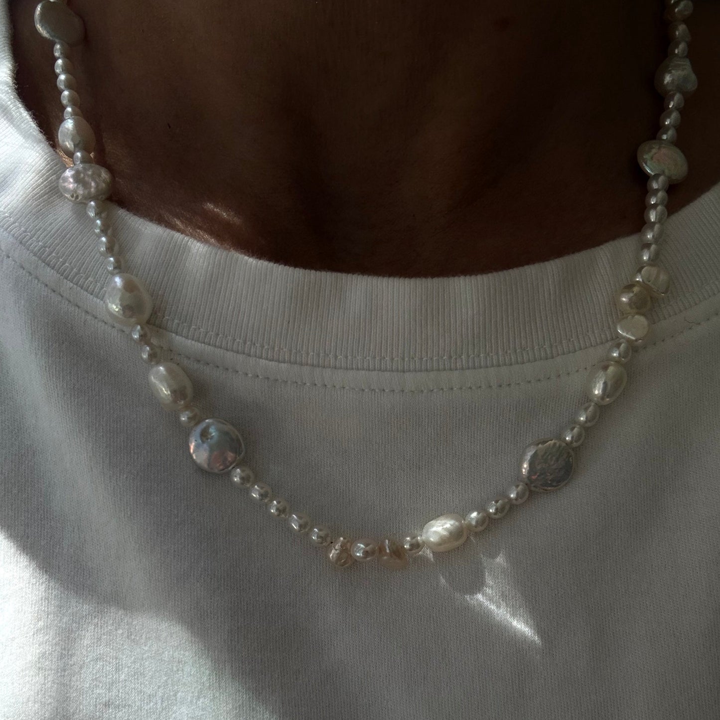Close-up of a pearl necklace on a white garment with a brown object partially visible.