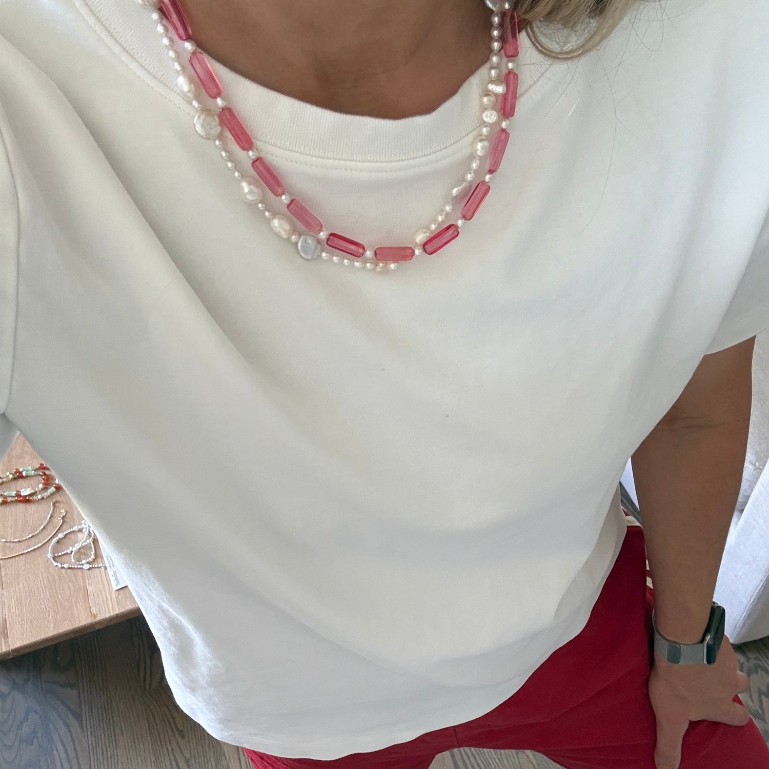 Person wearing a white dress with pink and pearl necklace on a wooden floor.