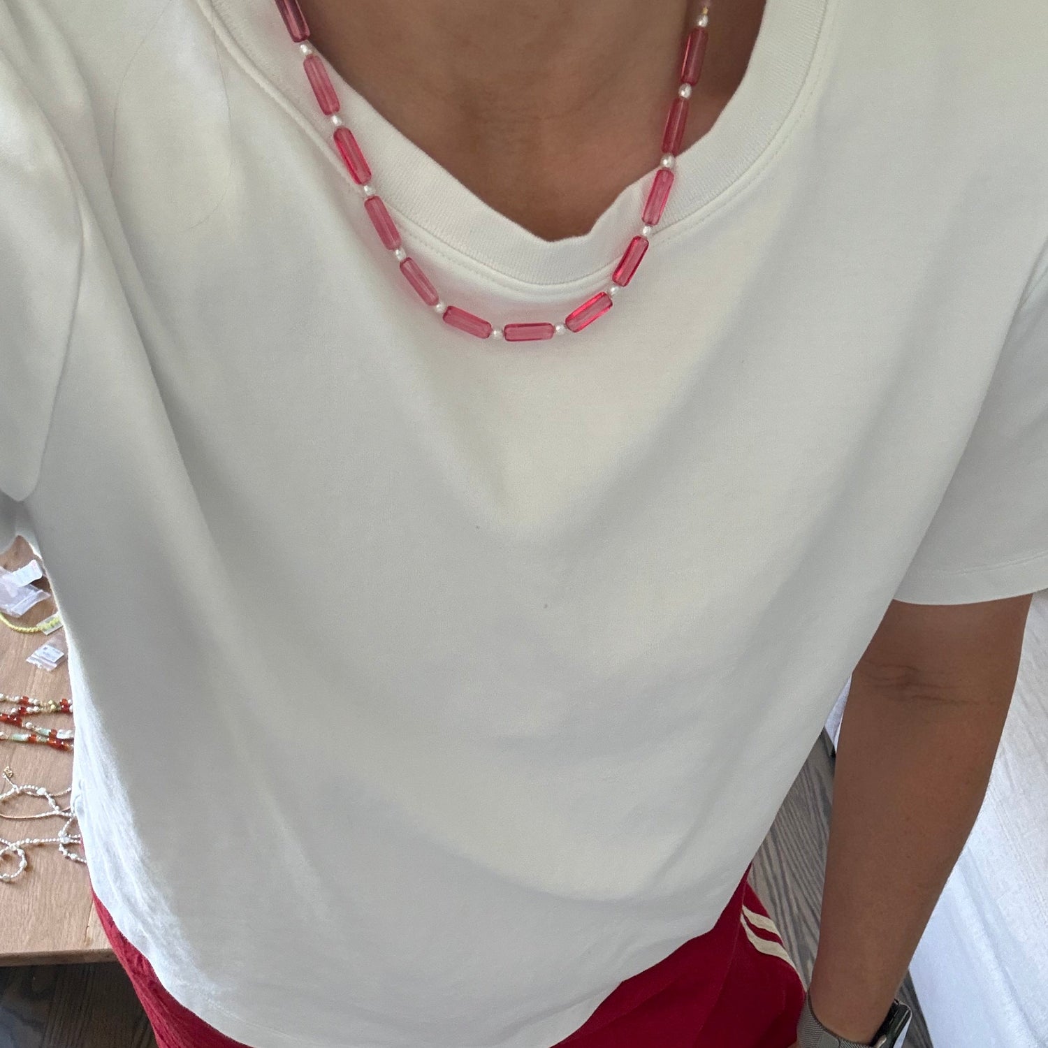 Person wearing a white top with pink accents and red pants on a wooden floor.