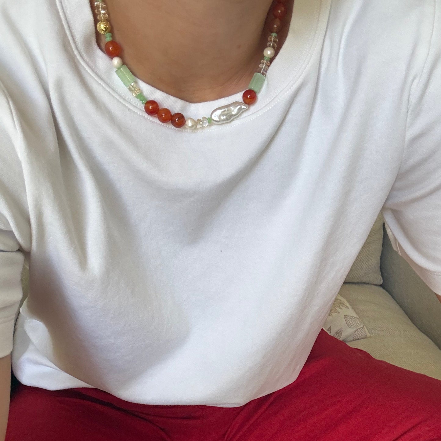 Close-up of a person wearing a white garment with a red sleeve and a beaded necklace.