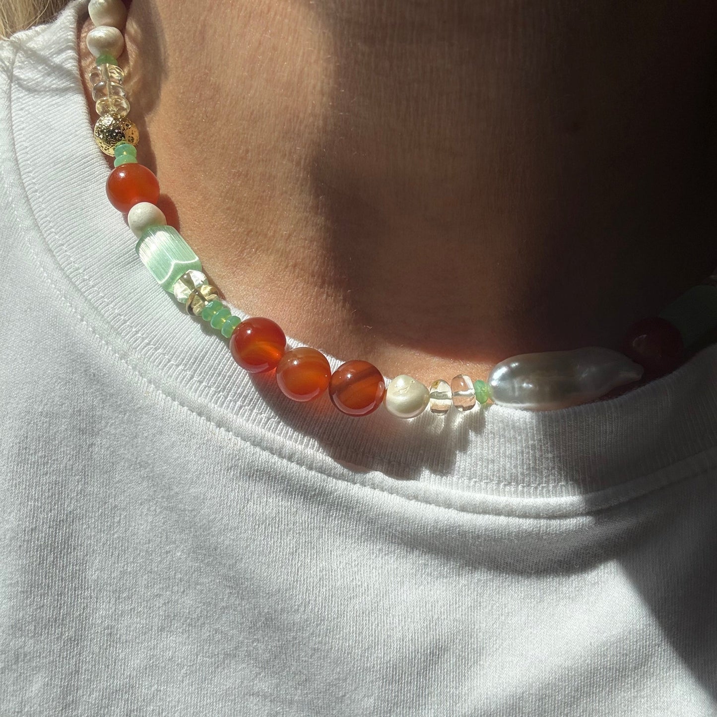 Close-up of a beaded necklace with multicolored beads on a white shirt.
