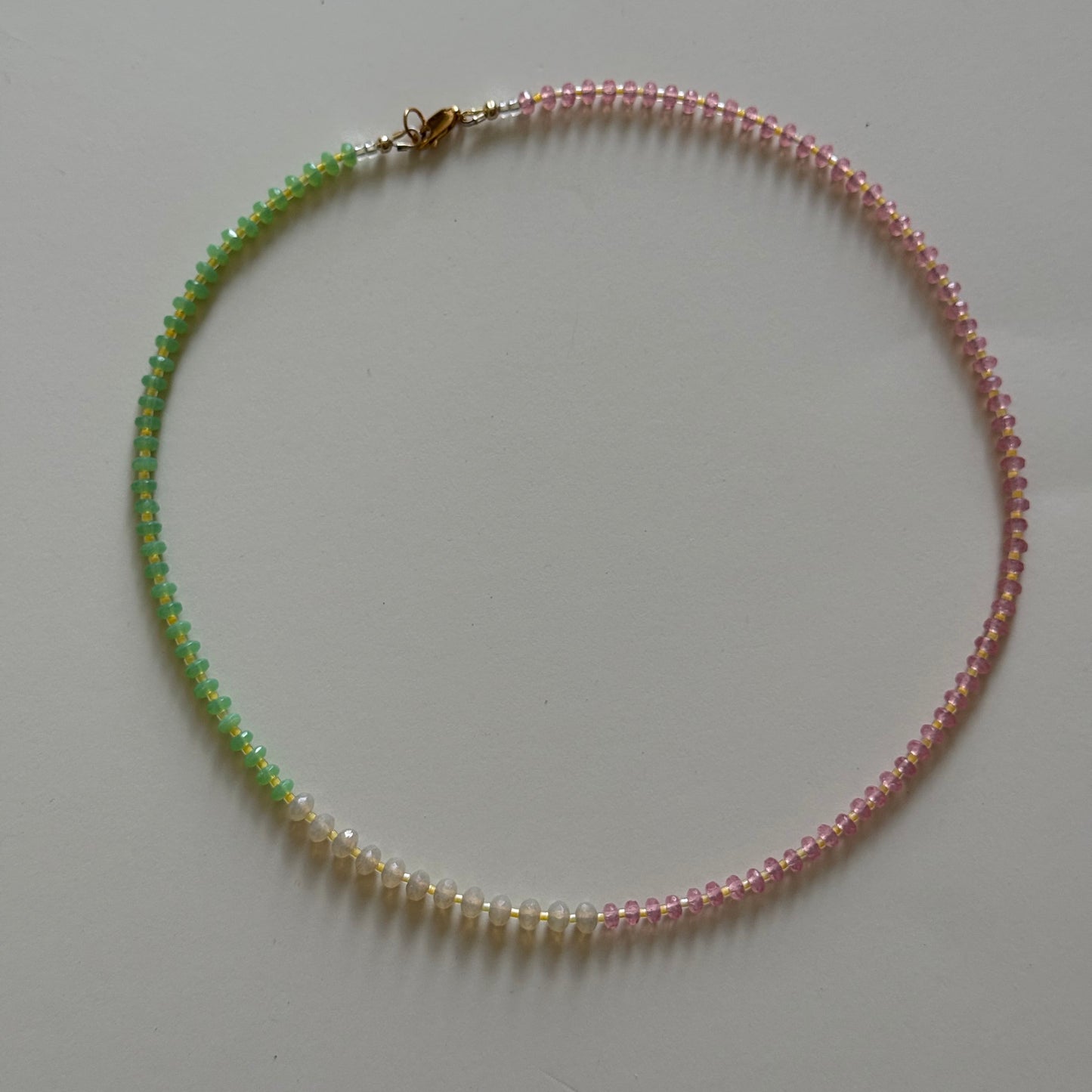 Necklace with alternating pink and green beads on a light gray background