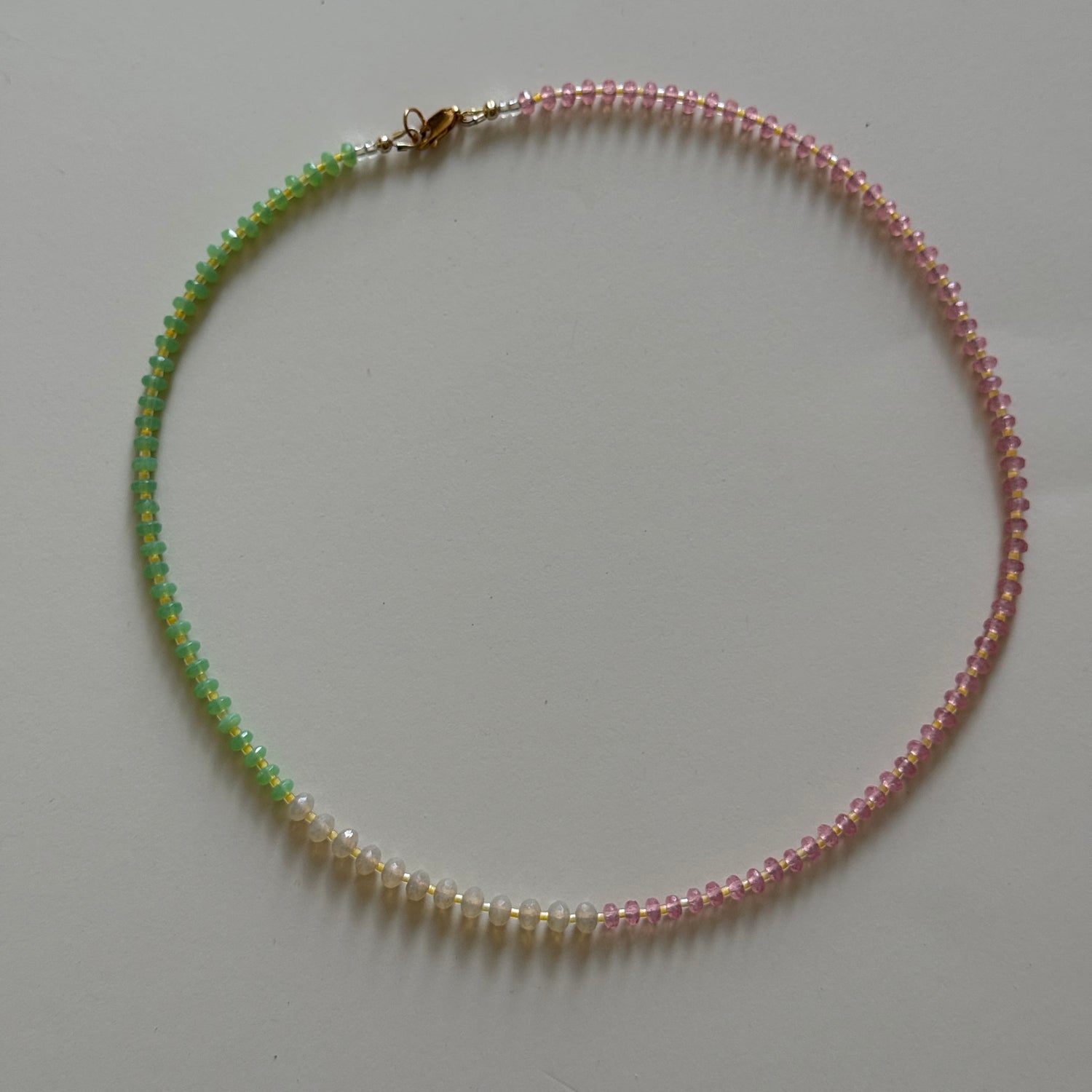 Necklace with alternating pink and green beads on a light gray background
