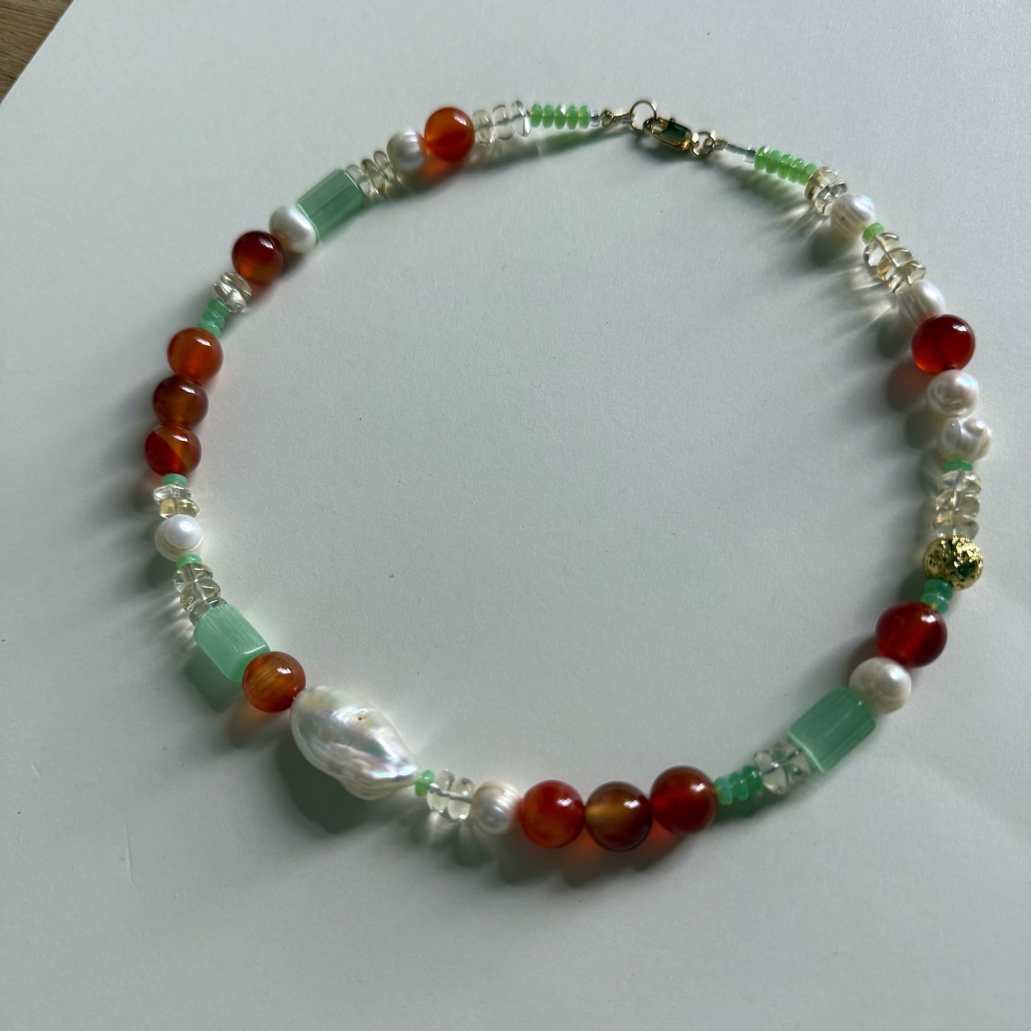 Beaded necklace with red, green, and white beads on a light gray background