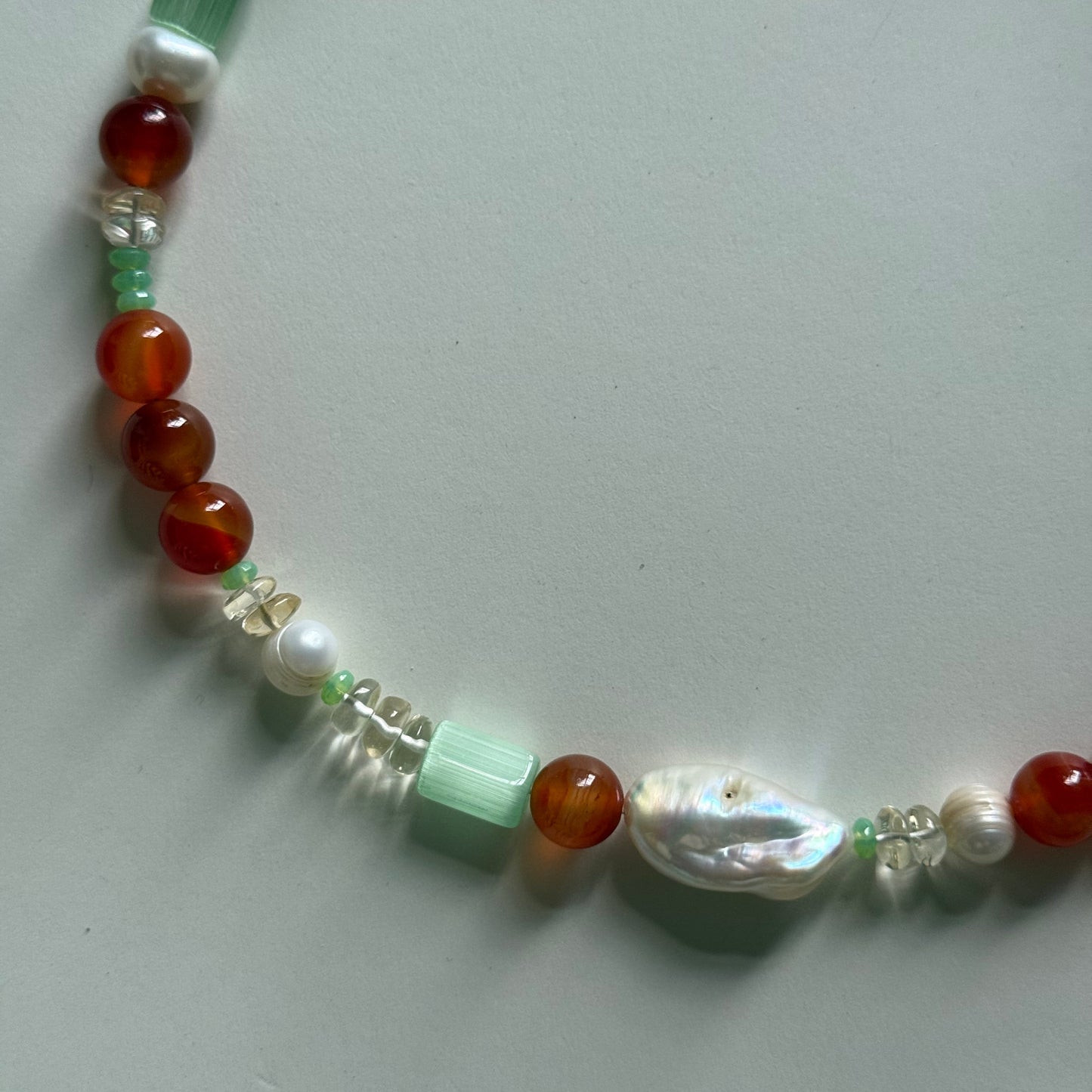 Beaded necklace with red, green, and white beads on a light gray background