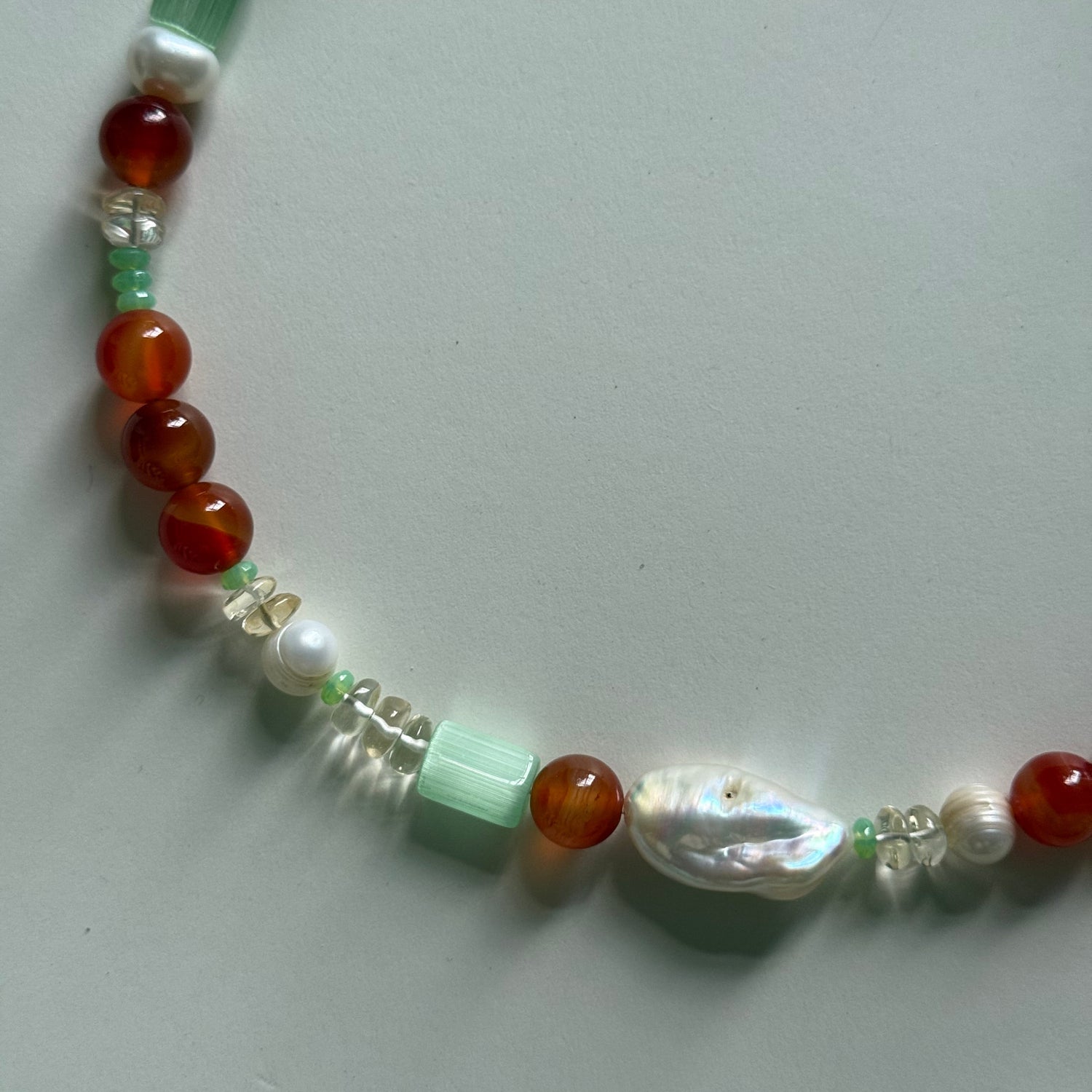 Beaded necklace with red, green, and white beads on a light gray background