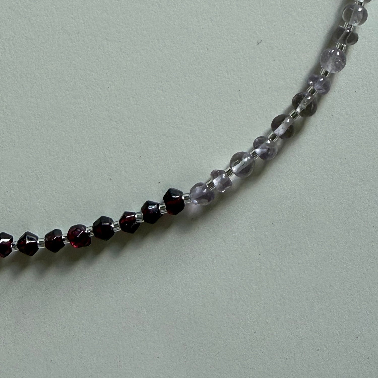 Close-up of a beaded necklace with alternating clear and black beads on a light gray background