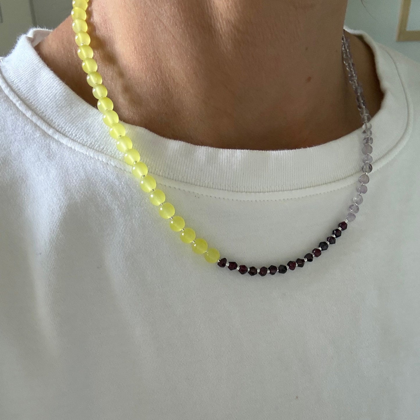 Close-up of a person wearing a beaded necklace with yellow beads on a plain background