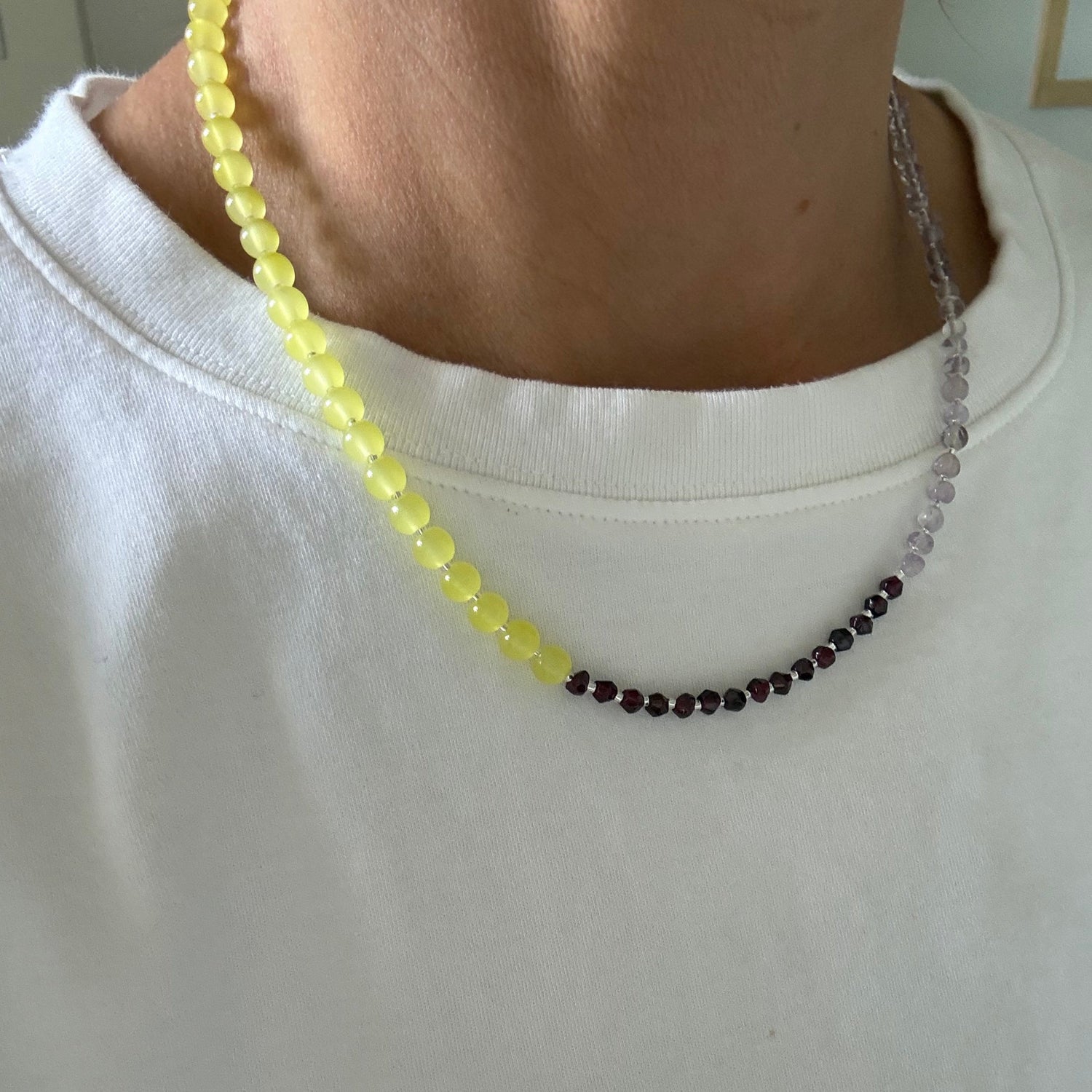 Close-up of a person wearing a beaded necklace with yellow beads on a plain background