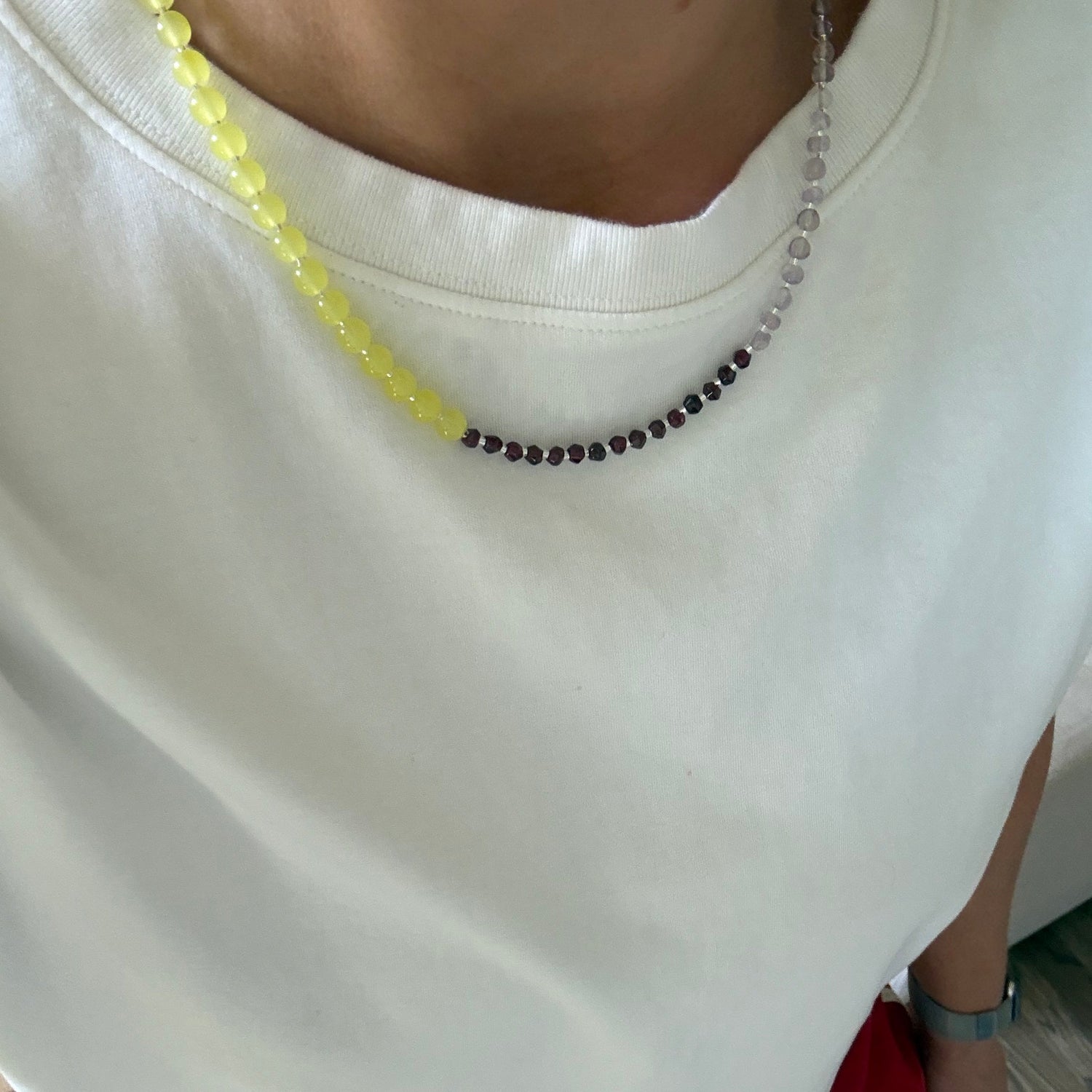 Close-up of a person wearing a white top with a beaded necklace, sitting on a red chair.