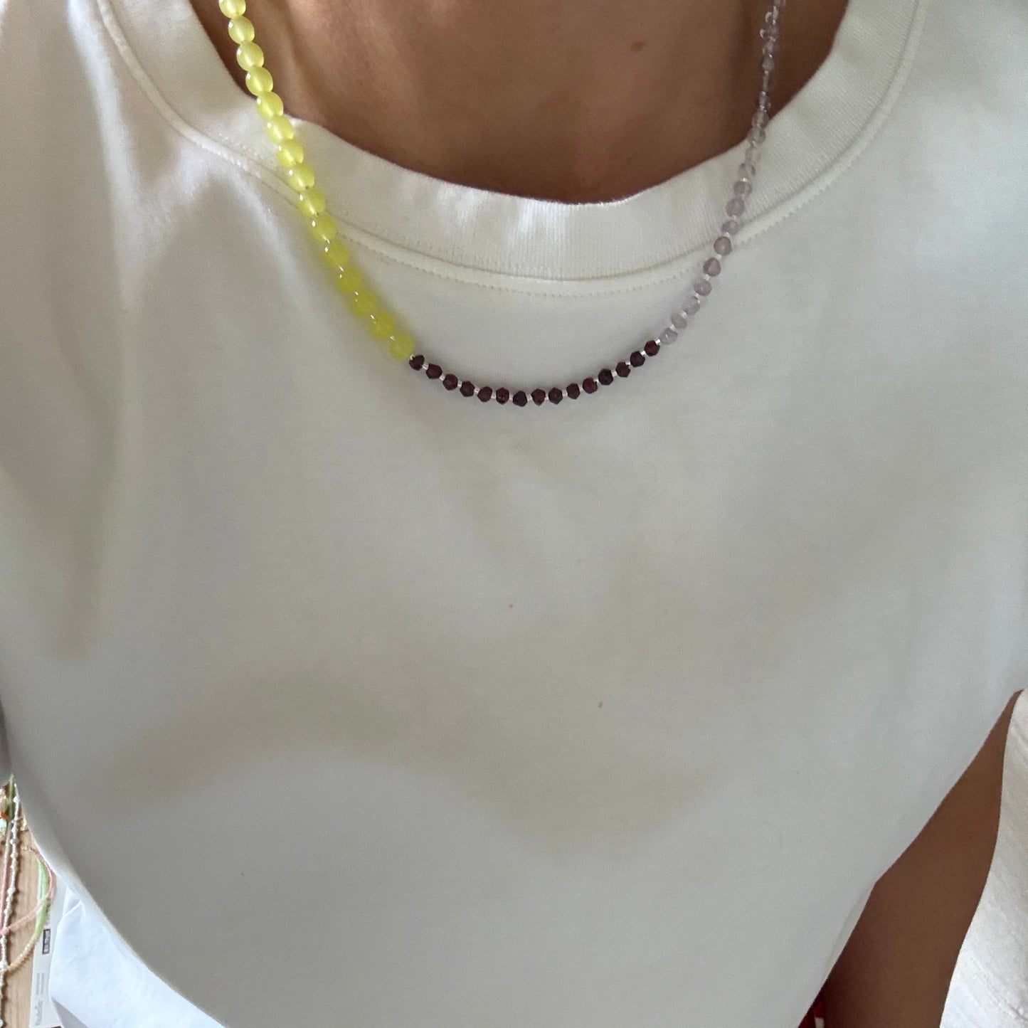 Close-up of a person wearing a white sleeveless top with a necklace, sitting on a red chair.
