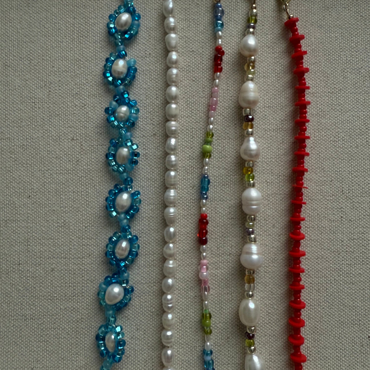 Four beaded bracelets in red, white, multicolor, and blue on a neutral background