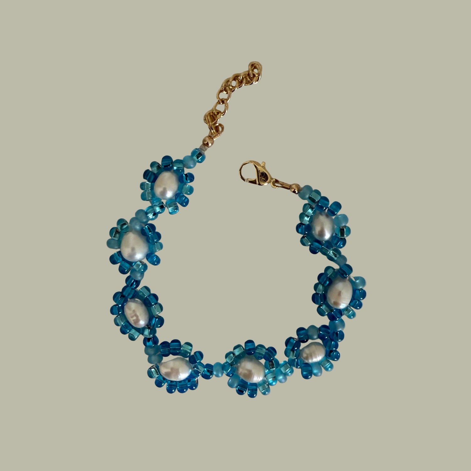 A bracelet with blue seed beads and pearls, featuring a gold-filled closure, displayed against a neutral background.