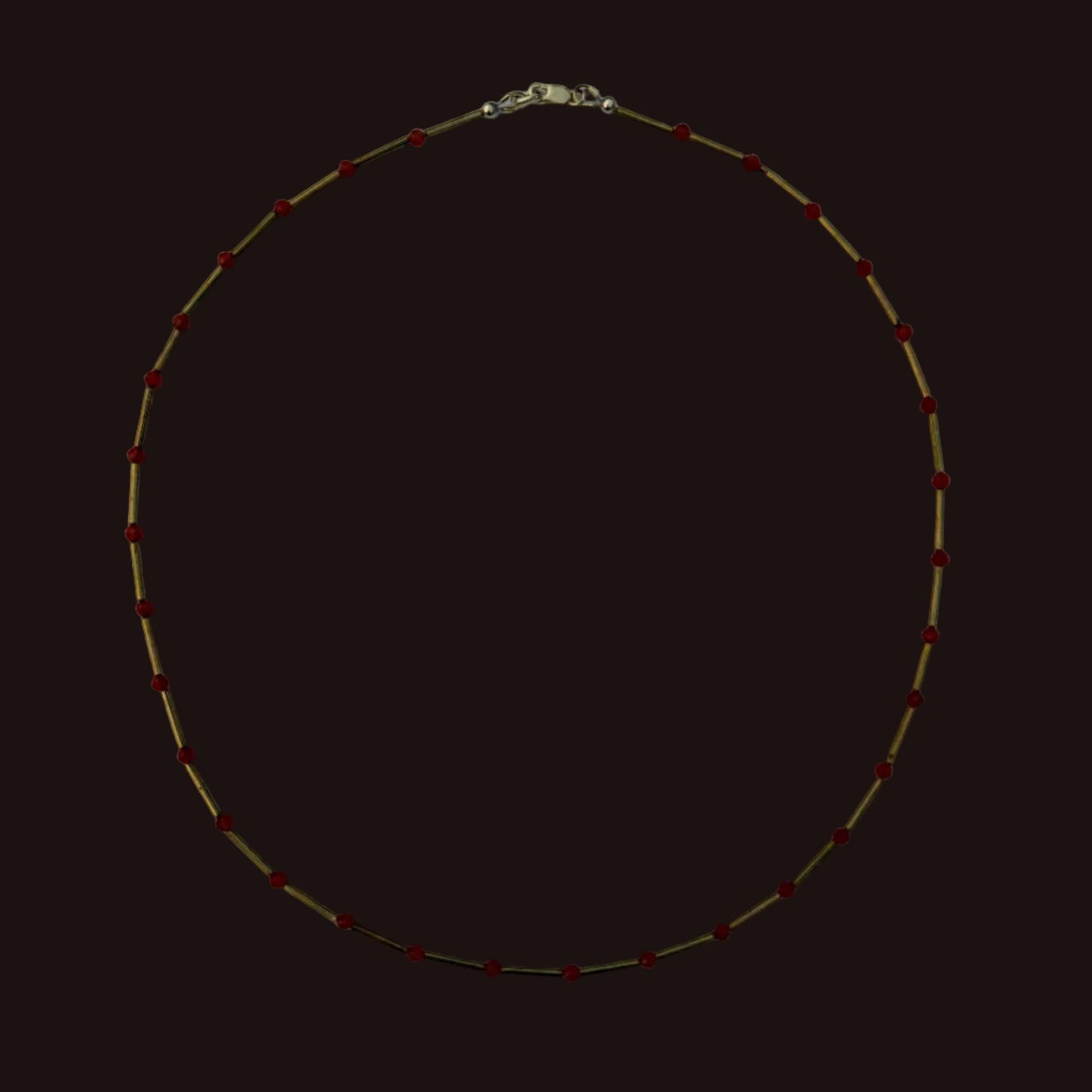 A delicate gold chain necklace with small, evenly spaced red beads, laid flat on a light gray background.