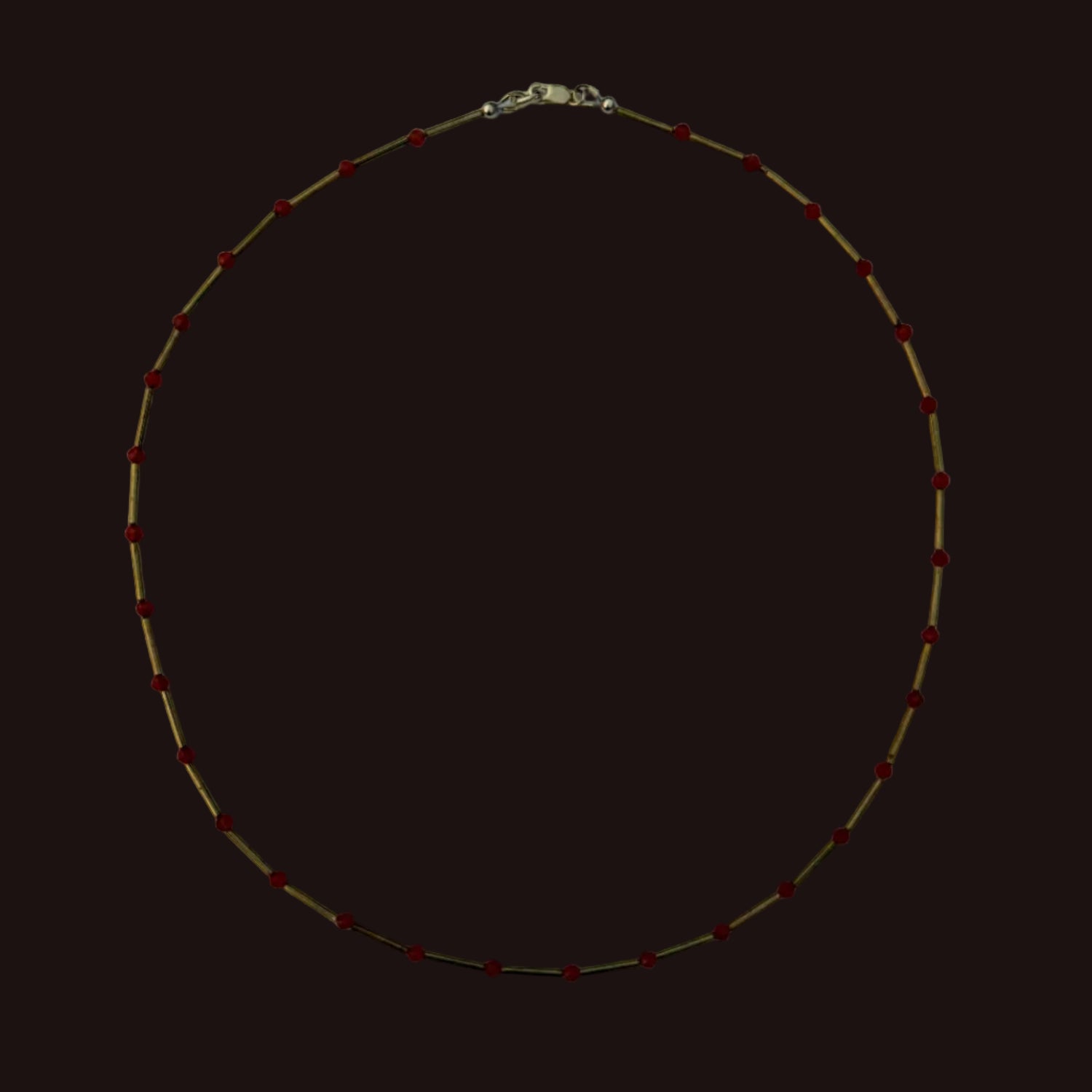 A delicate gold chain necklace with small, evenly spaced red beads, laid flat on a light gray background.