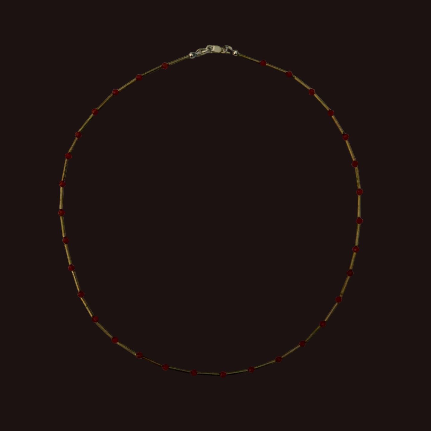 A delicate gold chain necklace with small red beads spaced evenly along the chain, laid flat on a light gray background.