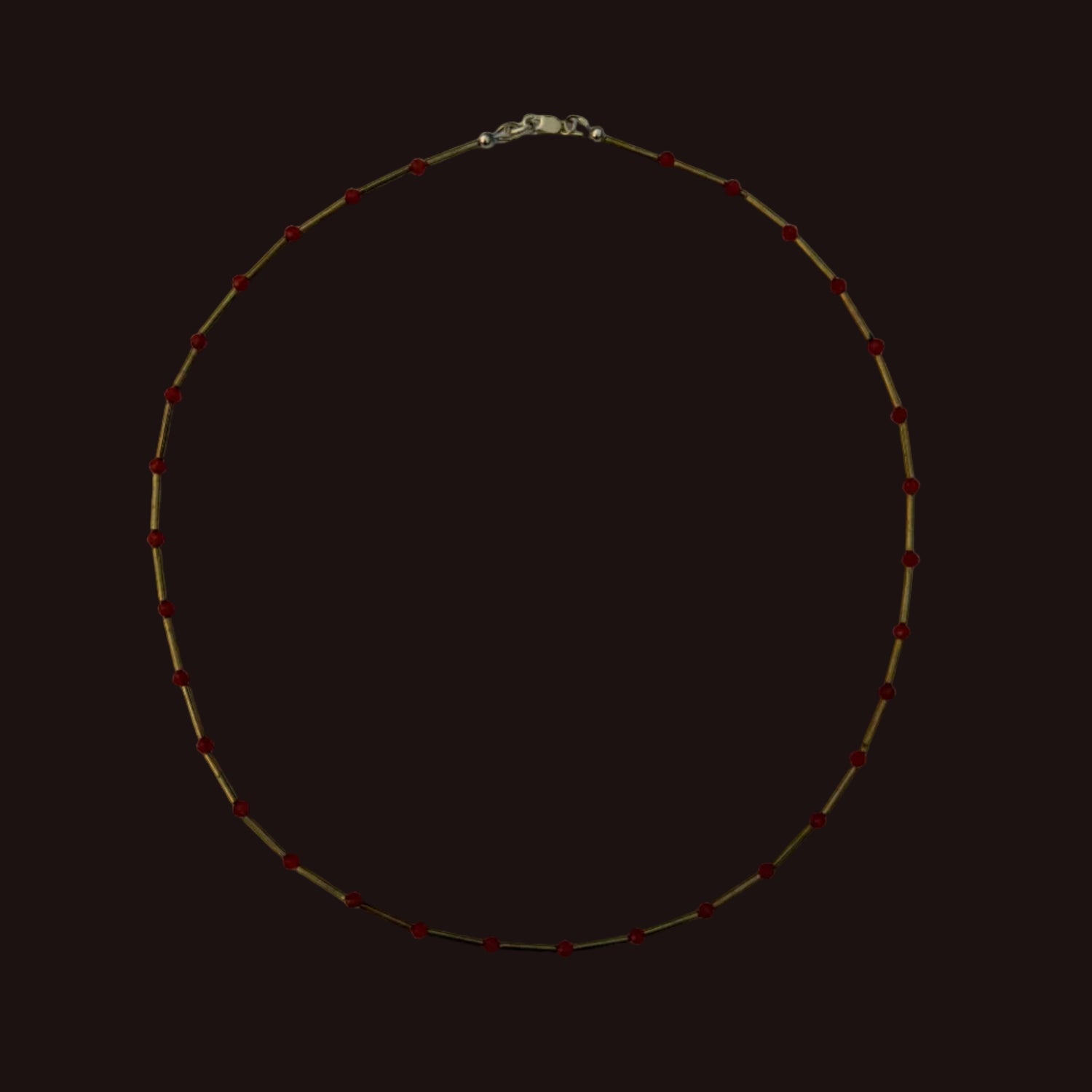 A delicate gold chain necklace with small red beads spaced evenly along the chain, laid flat on a light gray background.