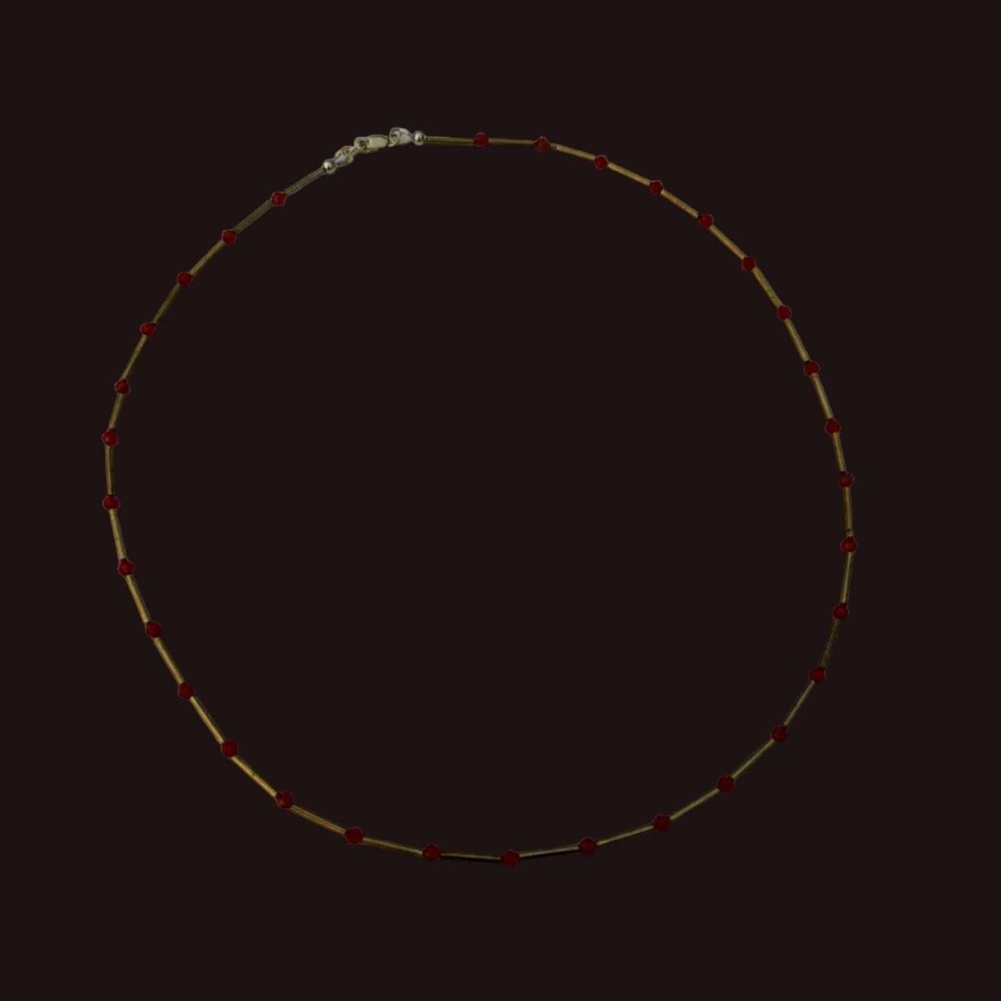 A delicate gold chain necklace with small red beads spaced evenly along the length, displayed on a plain white sheet of paper.