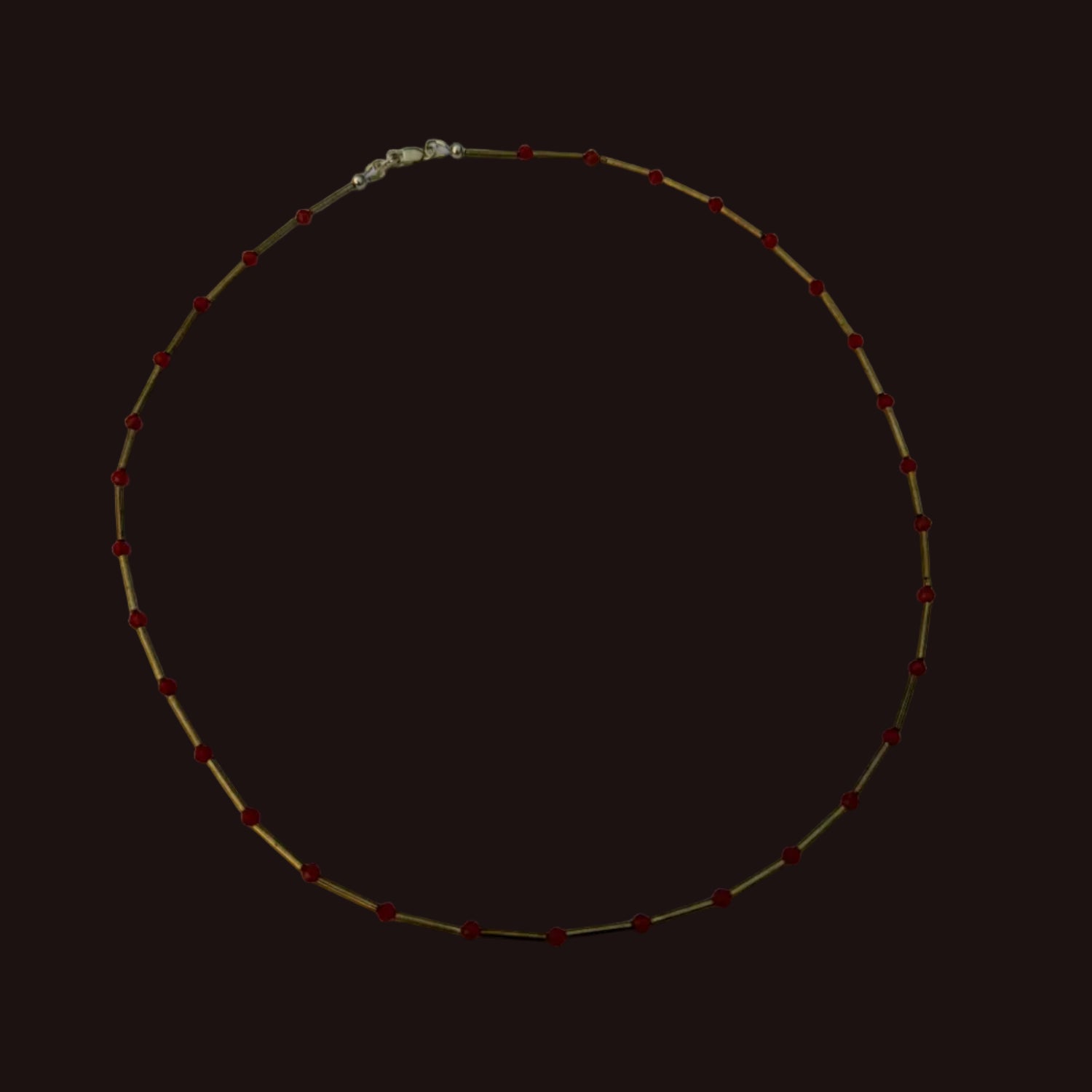 A delicate gold chain necklace with small red beads spaced evenly along the length, displayed on a plain white sheet of paper.