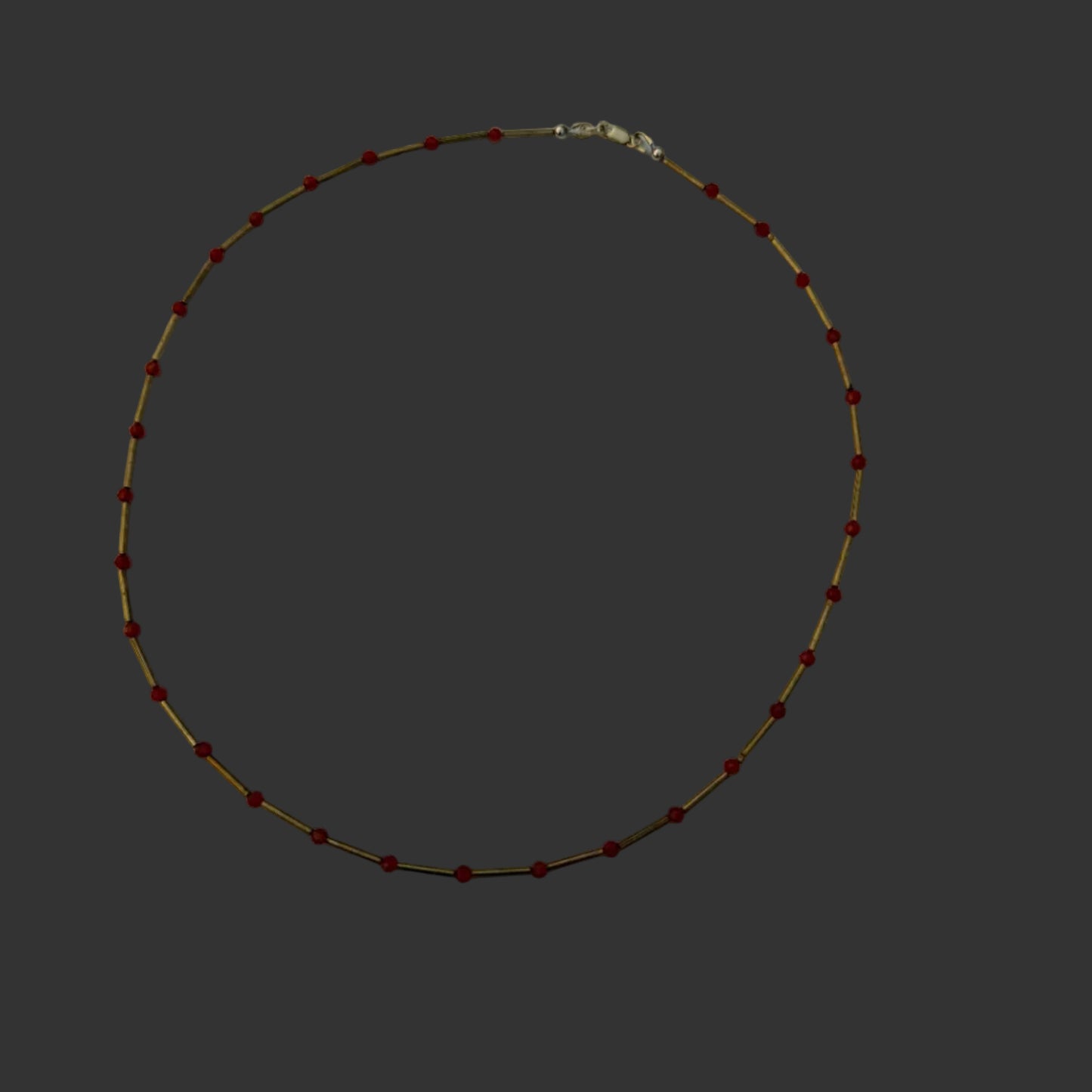 A delicate beaded necklace with small red beads and thin gold-toned links, arranged in a circle on a white sheet of paper.