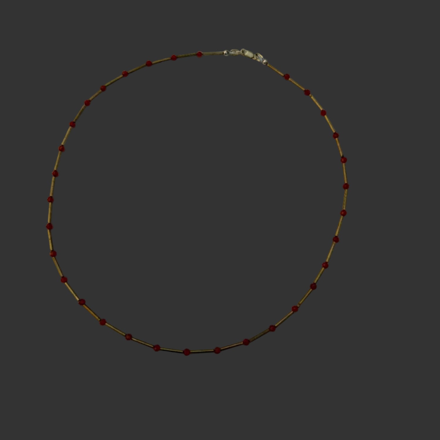 A delicate beaded necklace with small red beads and thin gold-toned links, arranged in a circle on a white sheet of paper.