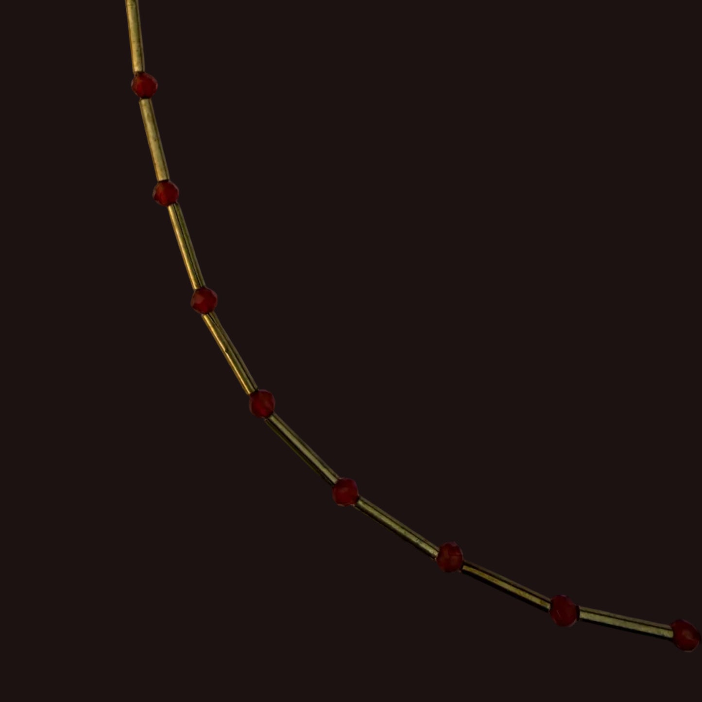 A close-up of a gold-toned chain or necklace with evenly spaced small red beads, photographed against a plain light background.