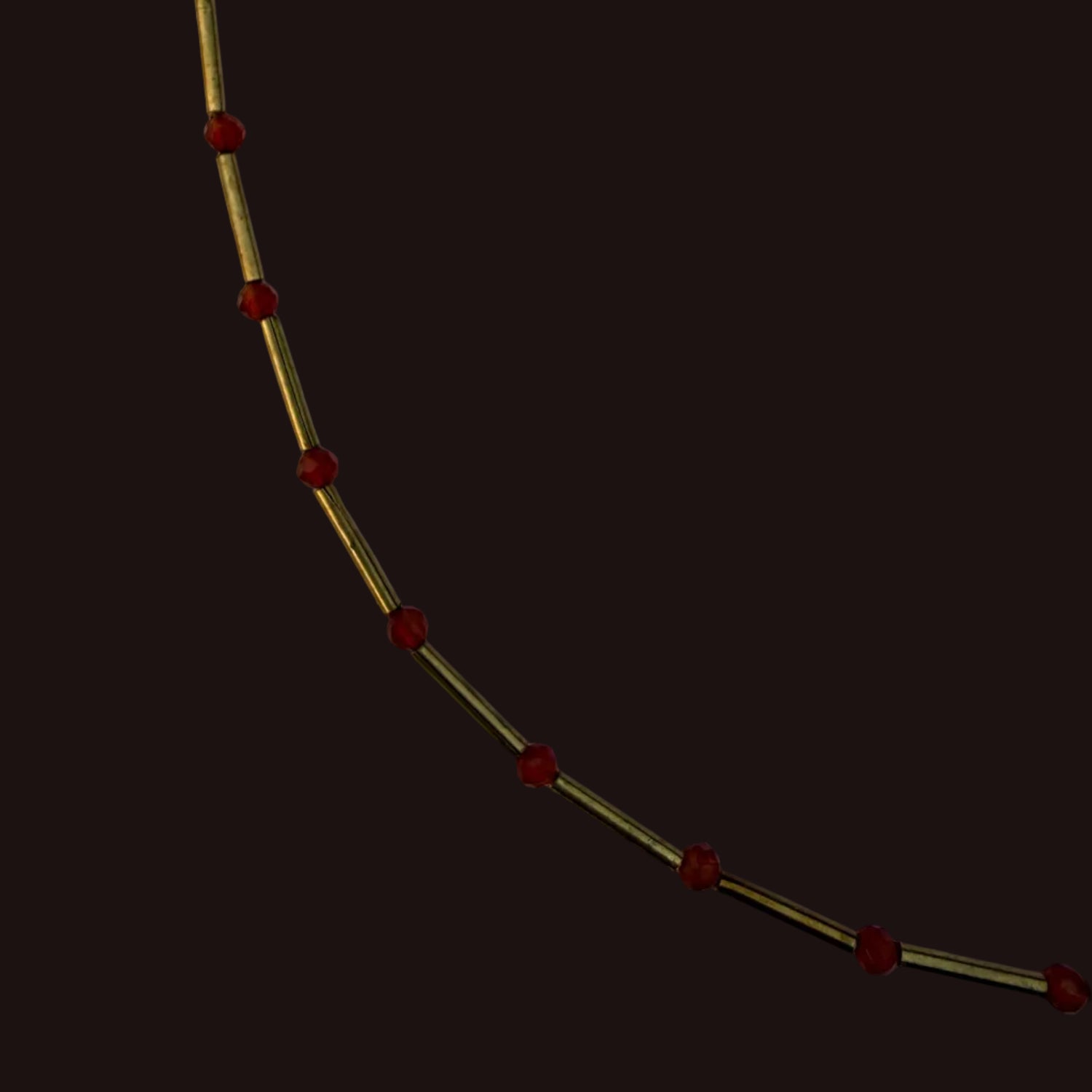 A close-up of a gold-toned chain or necklace with evenly spaced small red beads, photographed against a plain light background.