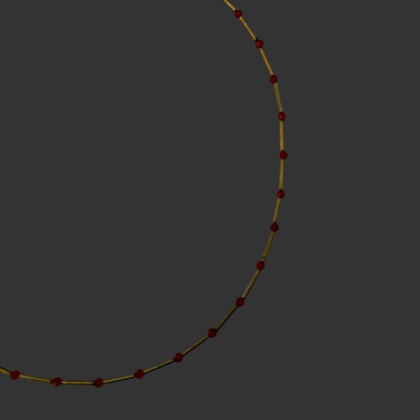 A delicate gold chain necklace with small, evenly spaced red beads, laid out in a semi-circle on a light gray background.