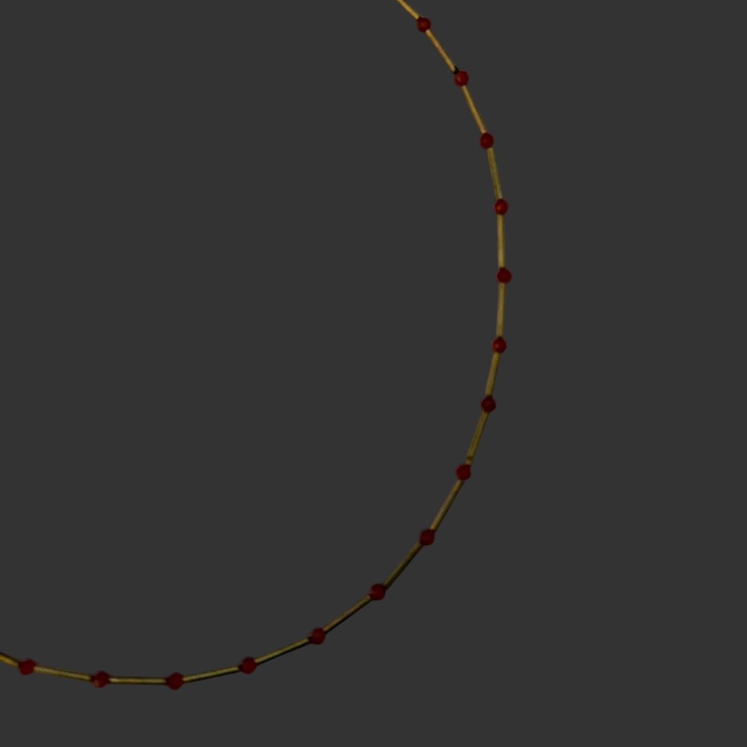 A delicate gold chain necklace with small, evenly spaced red beads, laid out in a semi-circle on a light gray background.