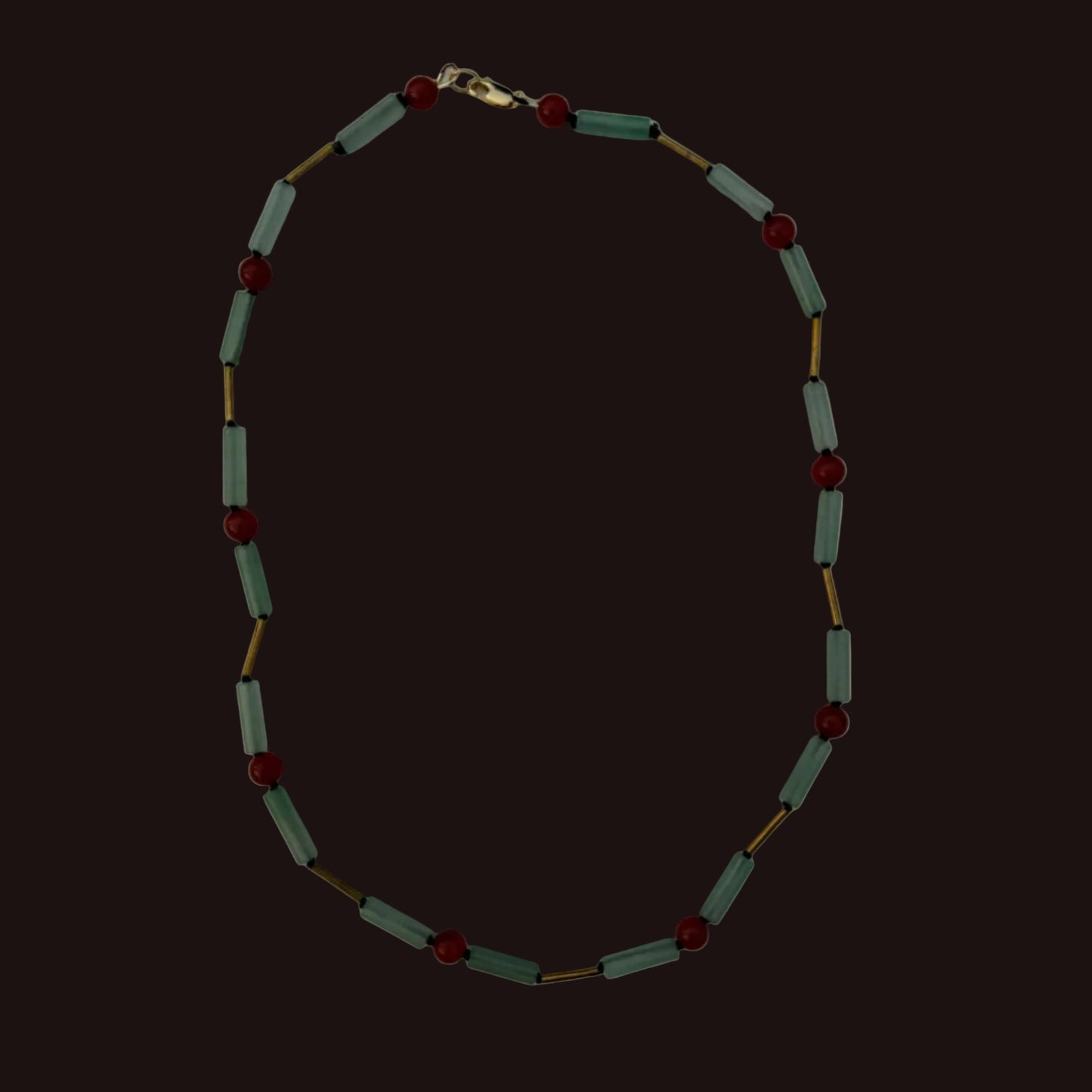 A beaded necklace featuring light sage green cylindrical beads and small dark red round beads, separated by thin gold-tone metal links, displayed on a plain light gray background.