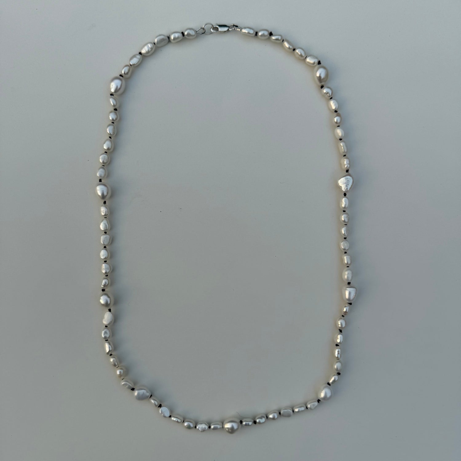 A silver beaded necklace with irregular, faceted beads, laid flat on a light gray surface.