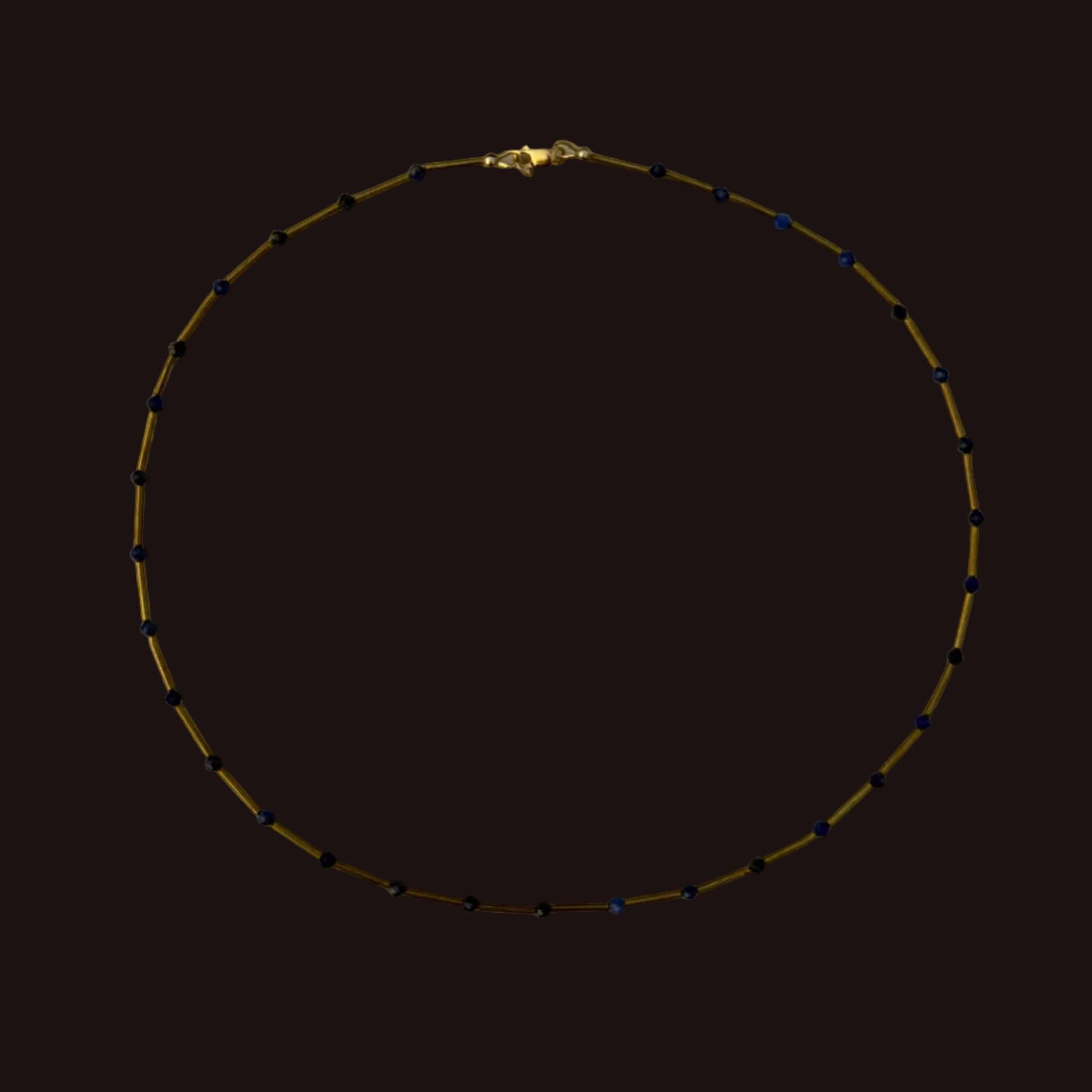 A delicate gold chain necklace with small dark blue beads spaced along the chain, displayed in a circle on a plain light gray background.
