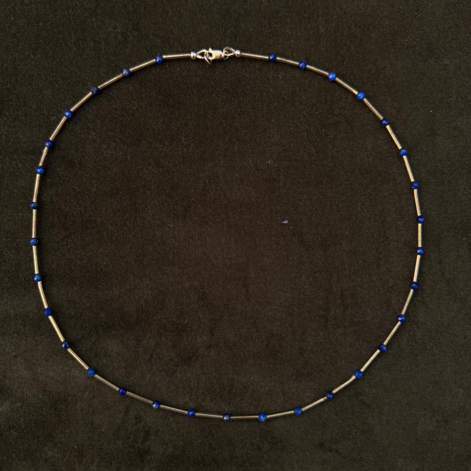 A delicate beaded necklace with small blue beads spaced along a thin silver-toned chain, displayed on a dark textured background.